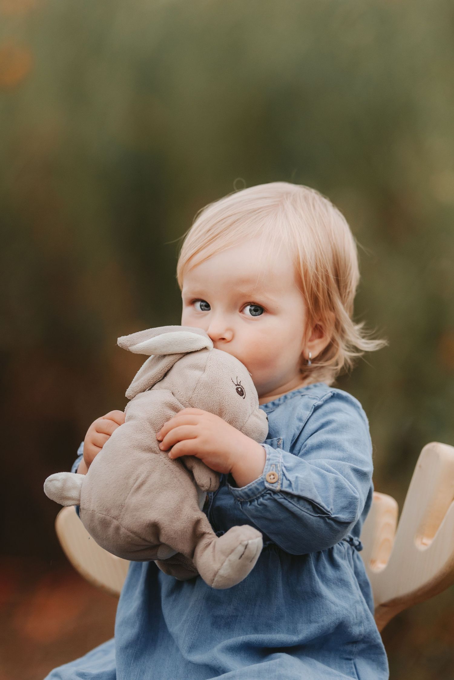Young child in blue dress holding gray stuffed bunny toy.