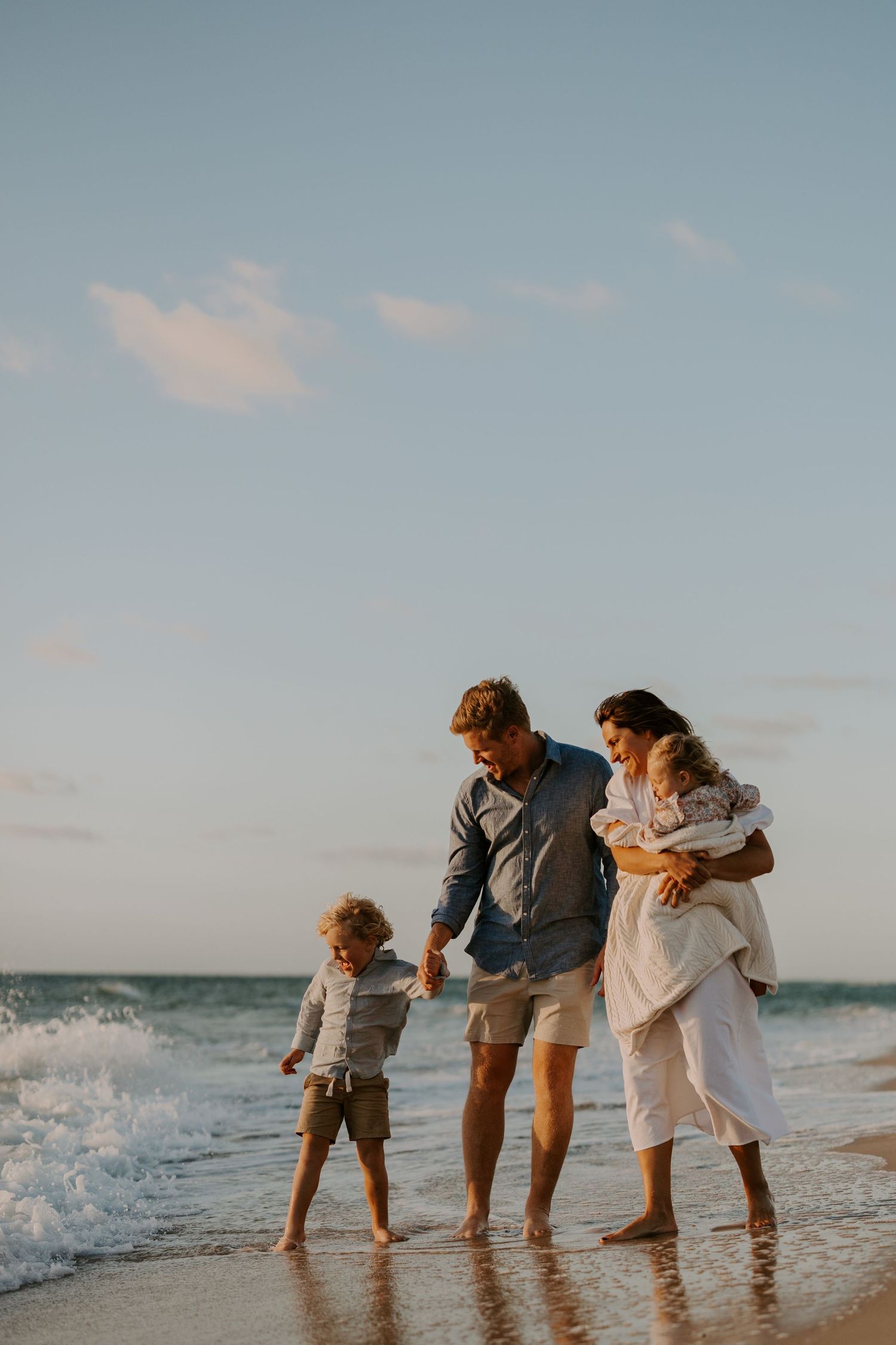 Family enjoying a sunset walk along the beach as waves crash at their feet.