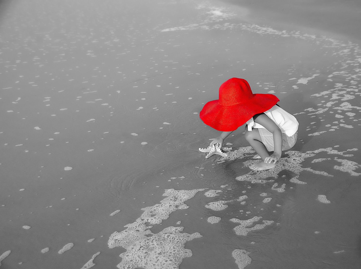 Black and white photo of child wearing red heart wings in water.