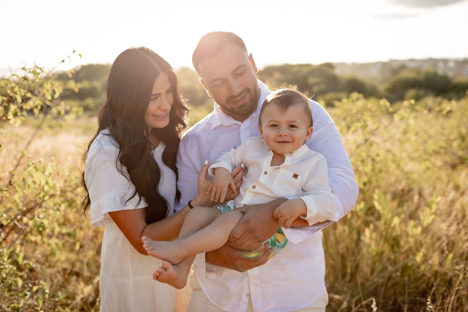 Family enjoying a tender moment together in a sunlit field during golden hour.