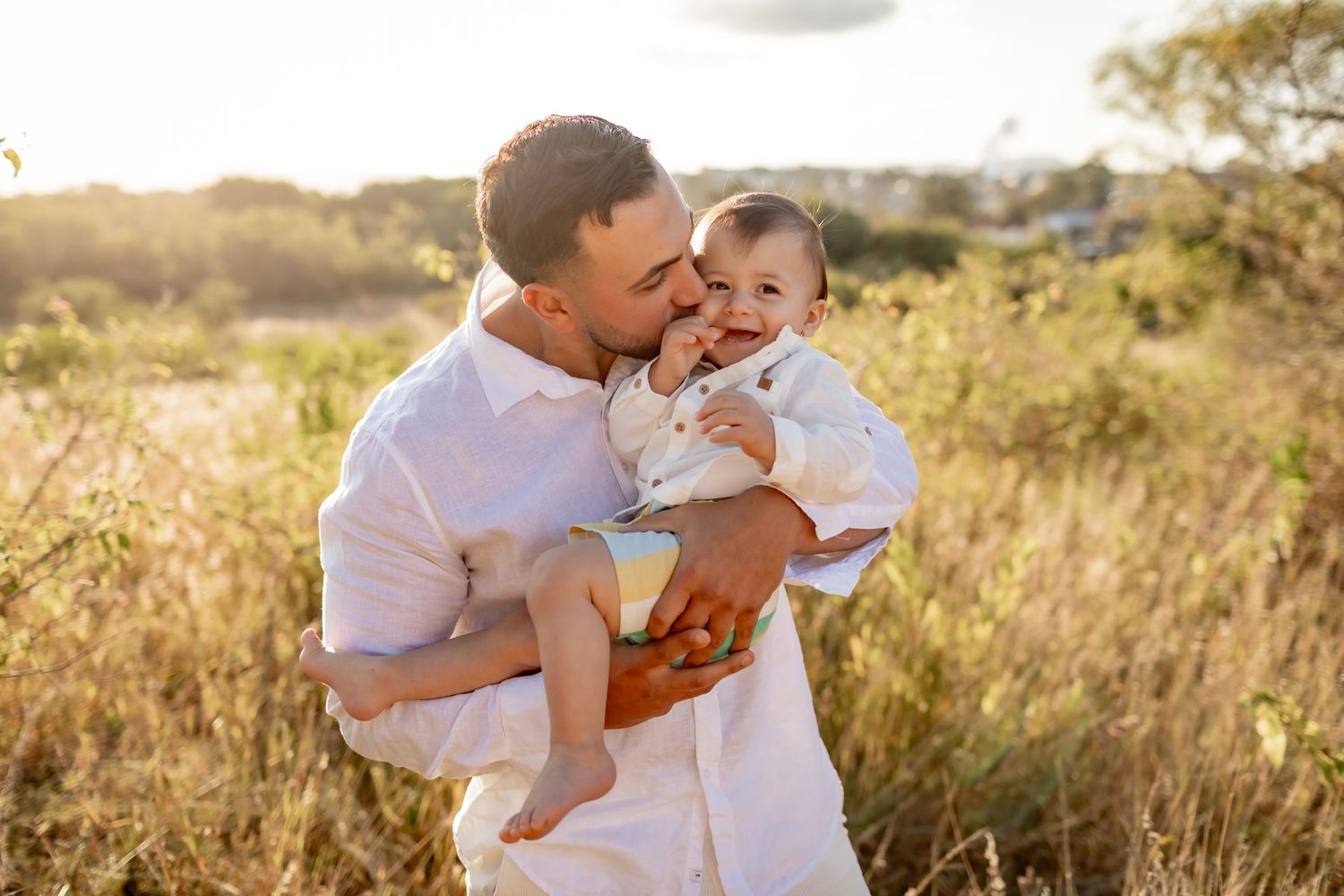 Parent and baby sharing a joyful close moment in a sunny field.