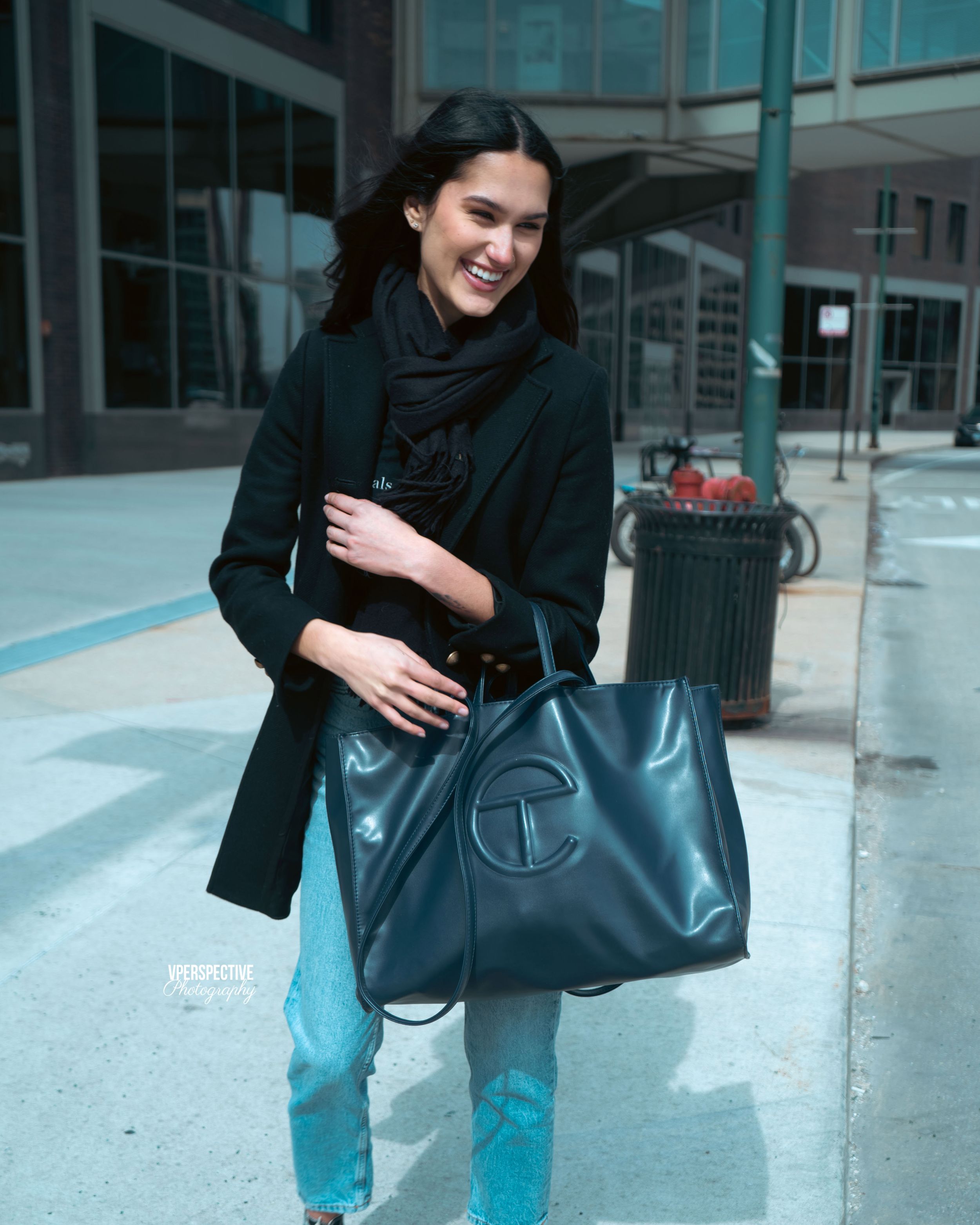 Street style fashion shot featuring a black coat and teal leather tote bag.