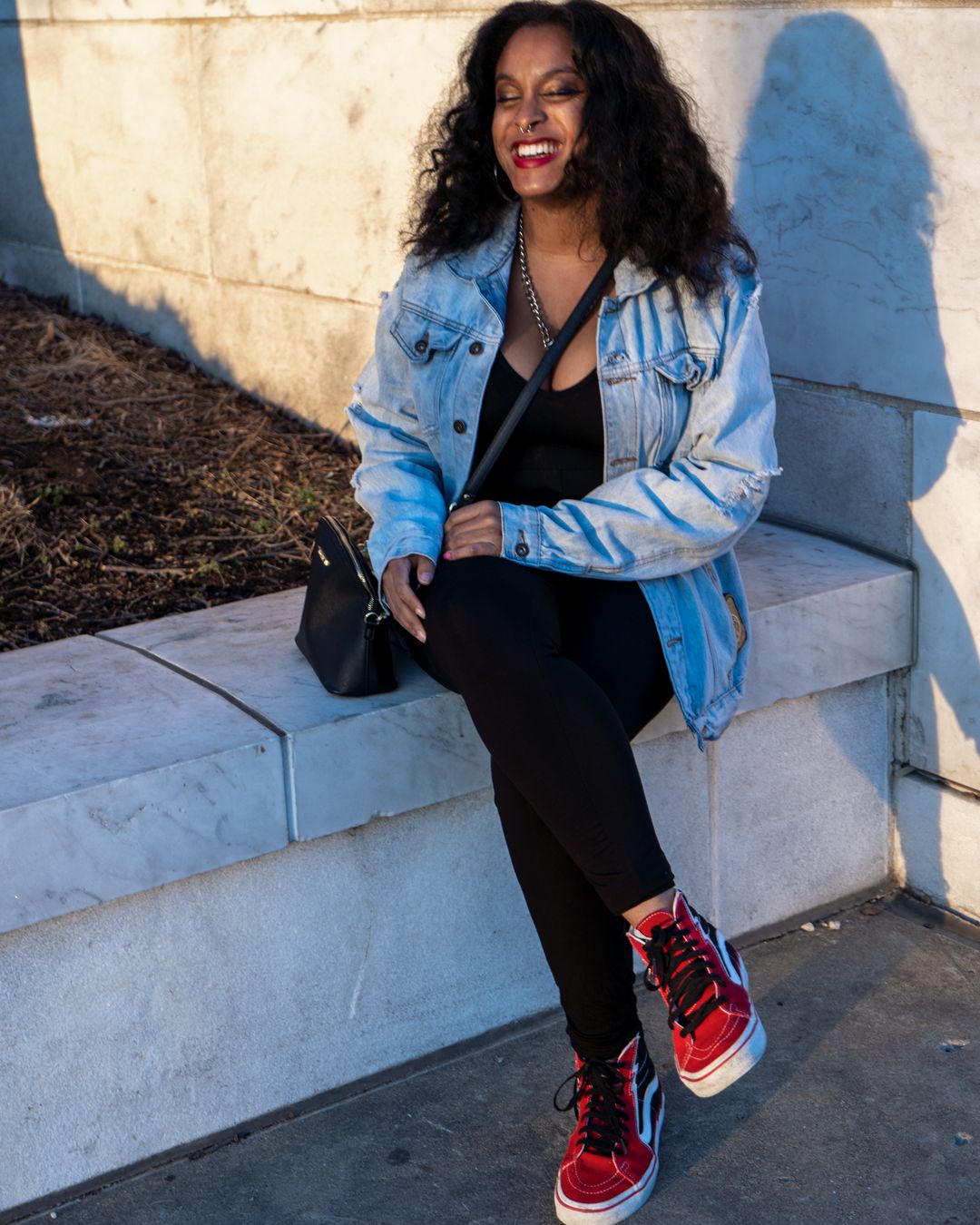 Casual street style outfit with denim jacket and red sneakers against white wall.