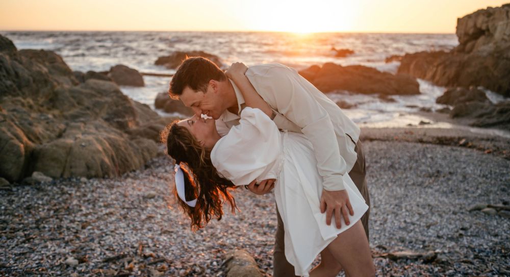 A romantic beach photoshoot during golden hour with rocky coastline in the background.