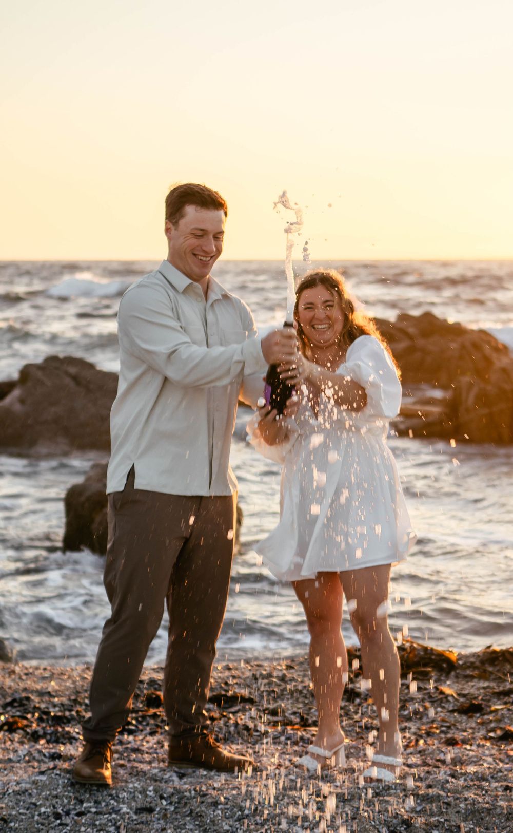 A couple plays and splashes in the ocean water during sunset.
