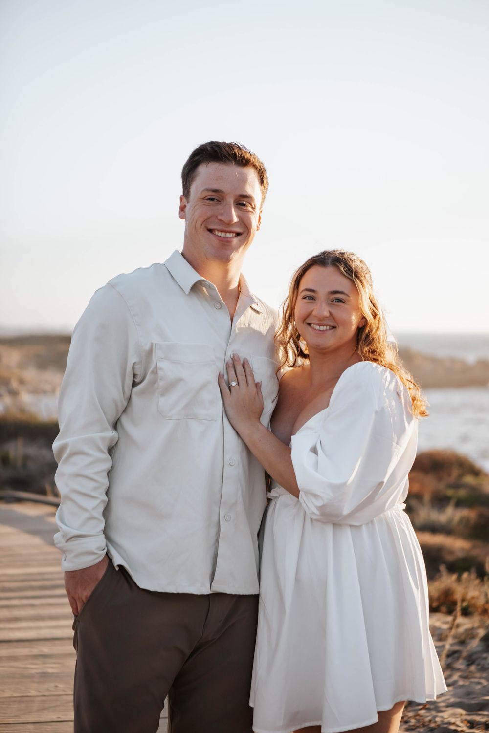 A couple shares a joyful moment together outdoors wearing coordinated white and brown outfits.