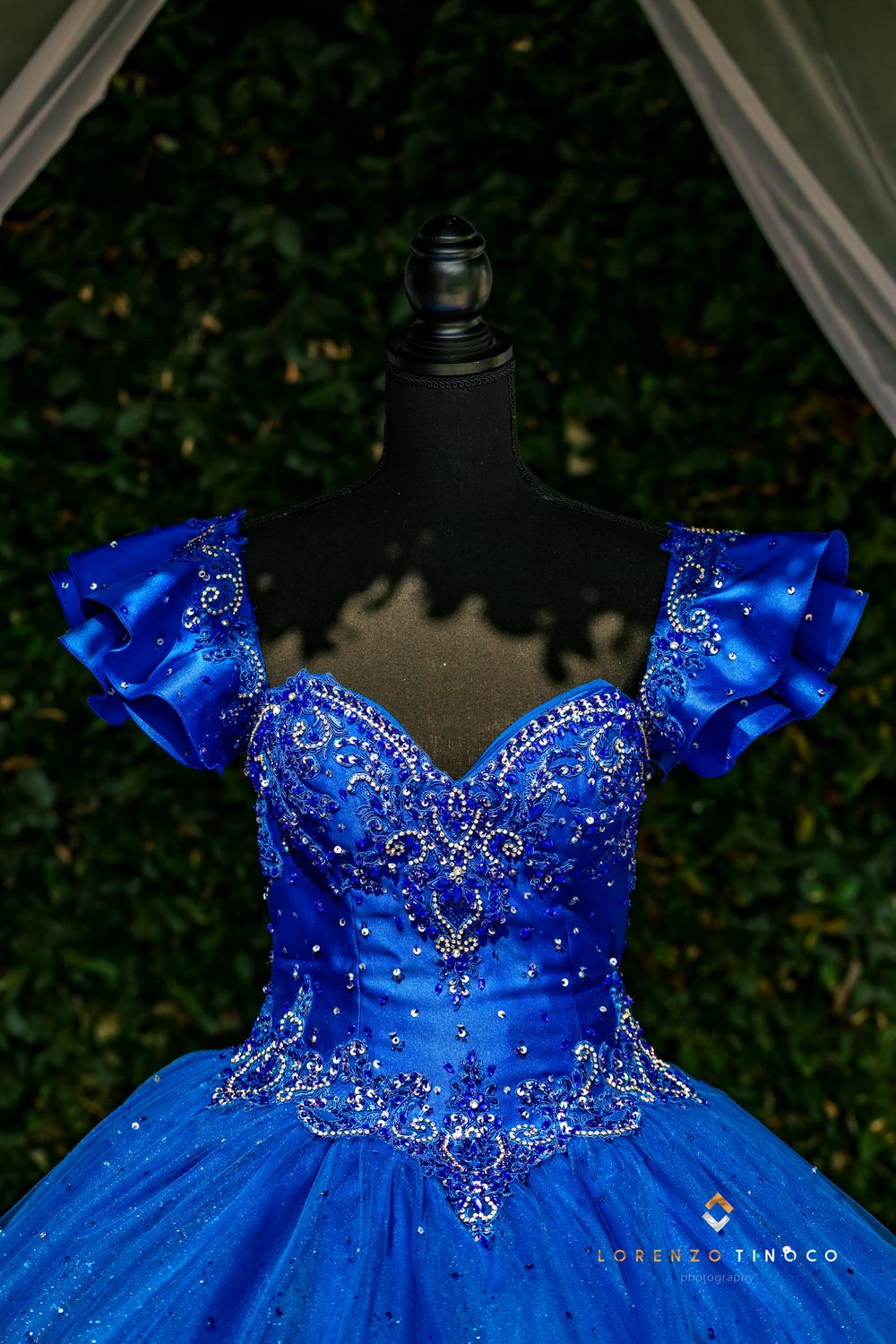 Close-up detail of a royal blue ball gown bodice with crystal embellishments on a dress form.