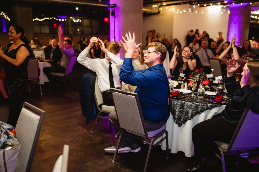 Wedding reception guests dancing and celebrating with colorful purple lighting in the background.