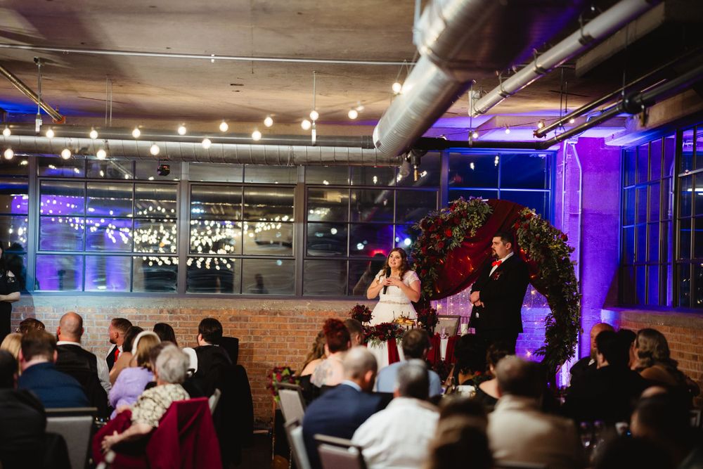 Wedding reception in an industrial venue with exposed brick walls and purple uplighting as guests watch the celebration.