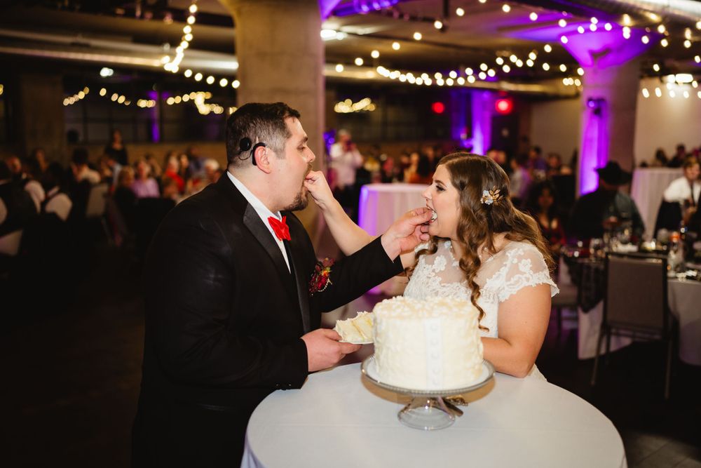 Newlyweds playfully feed each other wedding cake during their reception celebration.