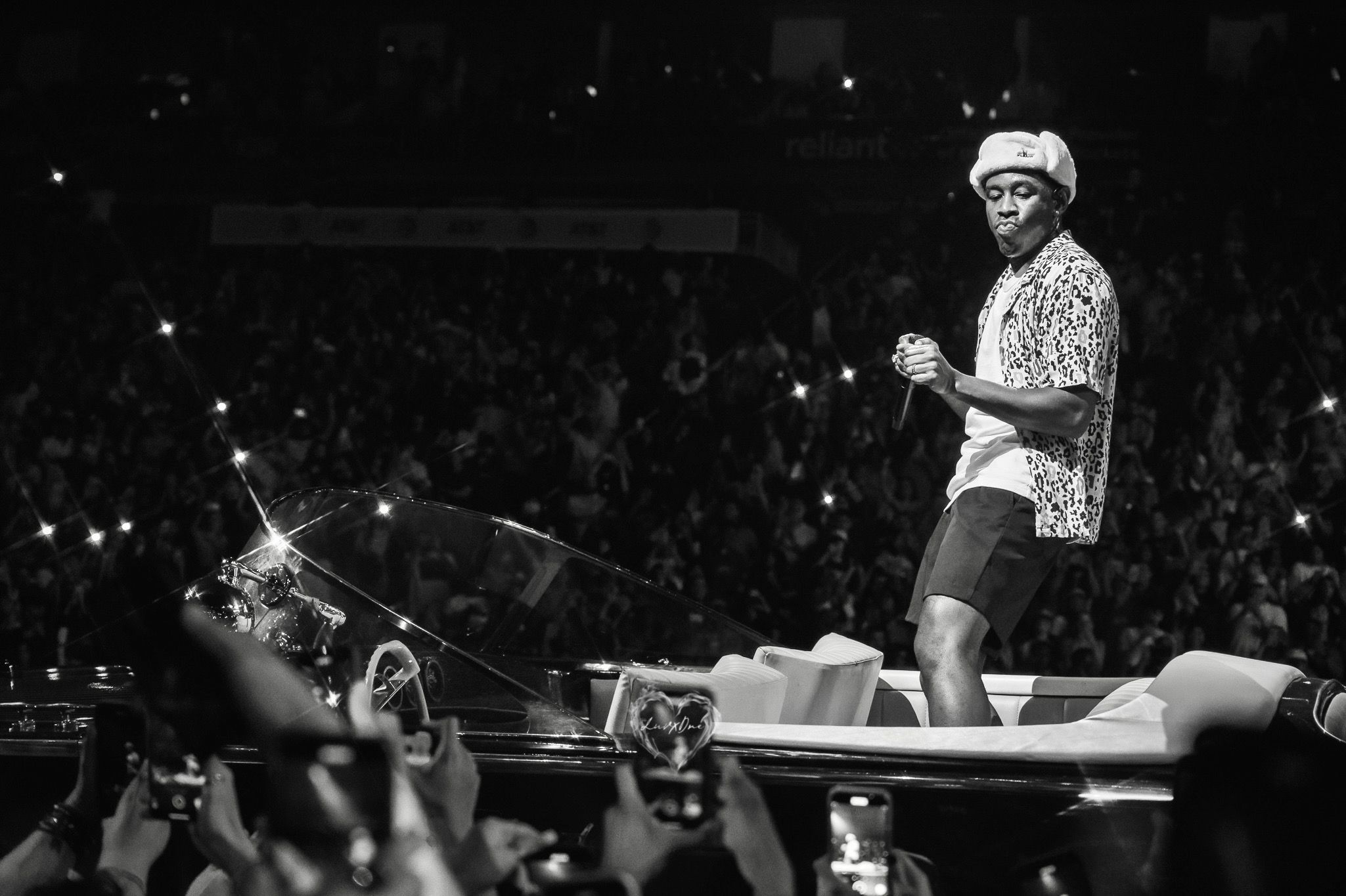 Black and white concert photo showing performer on stage with crowd in background.