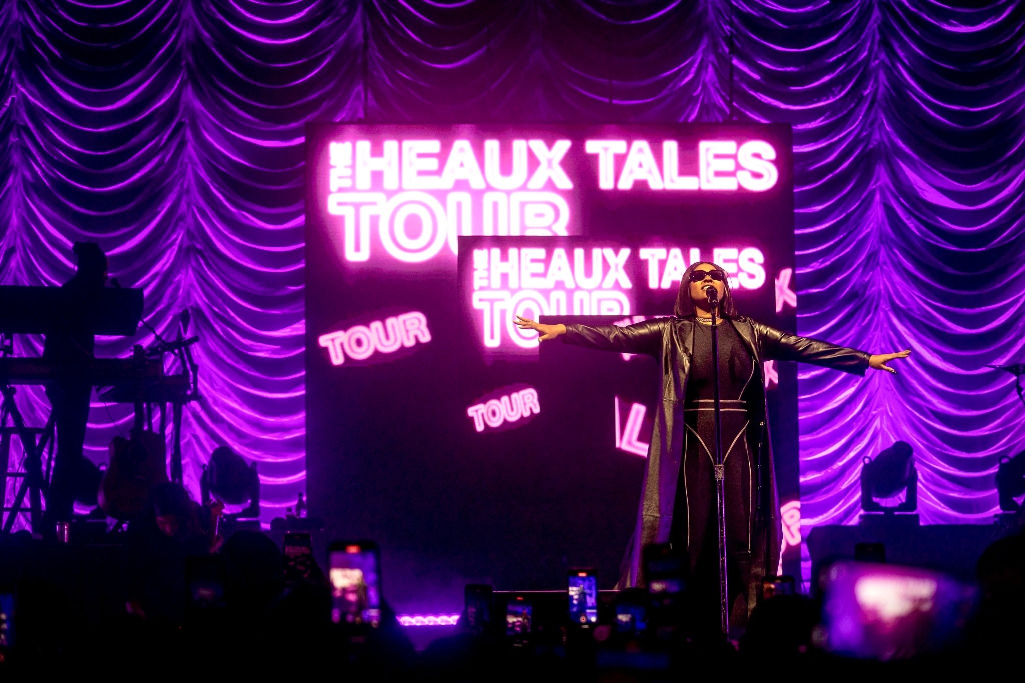 Purple-lit stage with neon 'Heaux Tales Tour' signage during live performance.