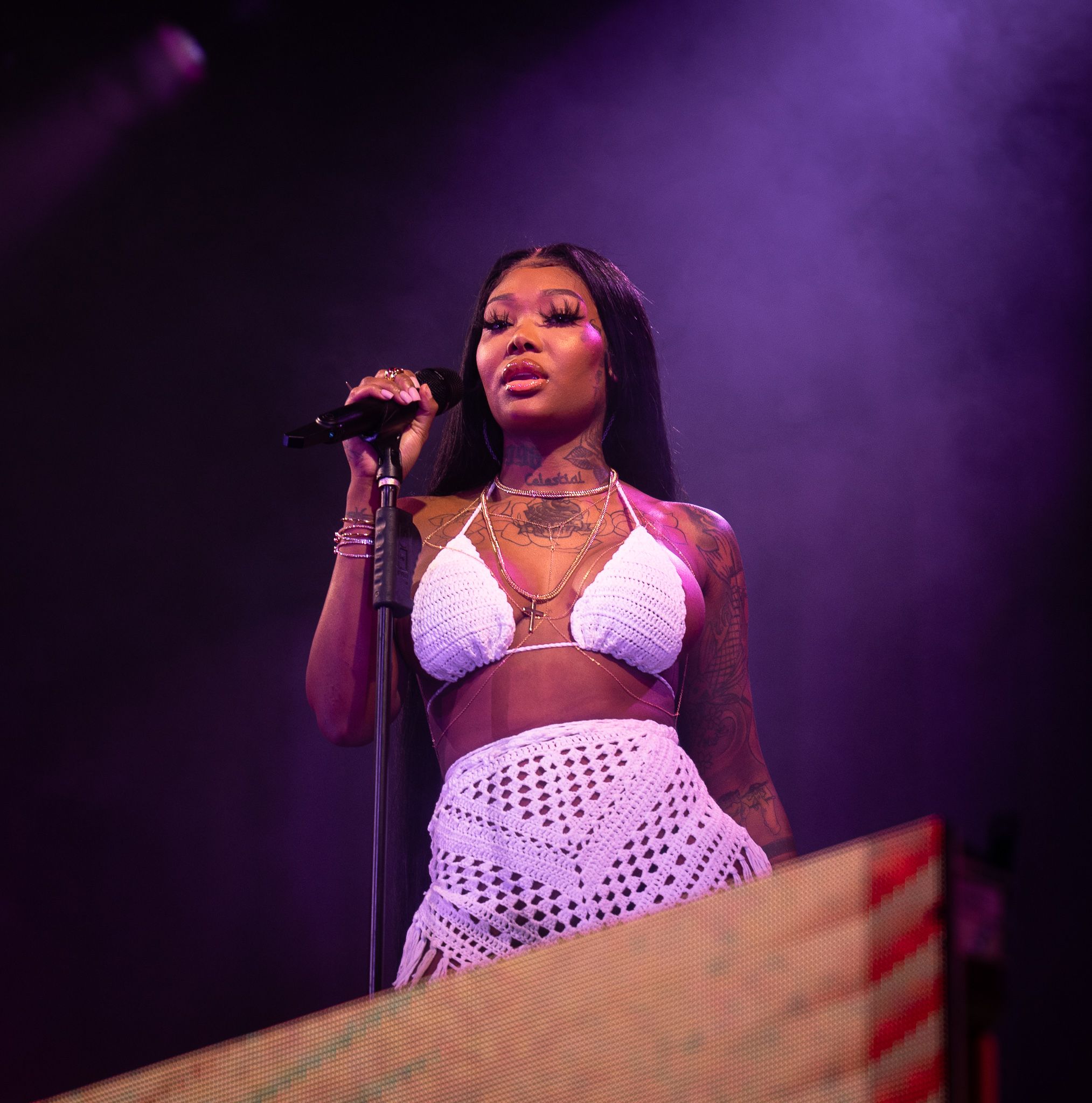 Singer performing on stage in white outfit under purple concert lighting.