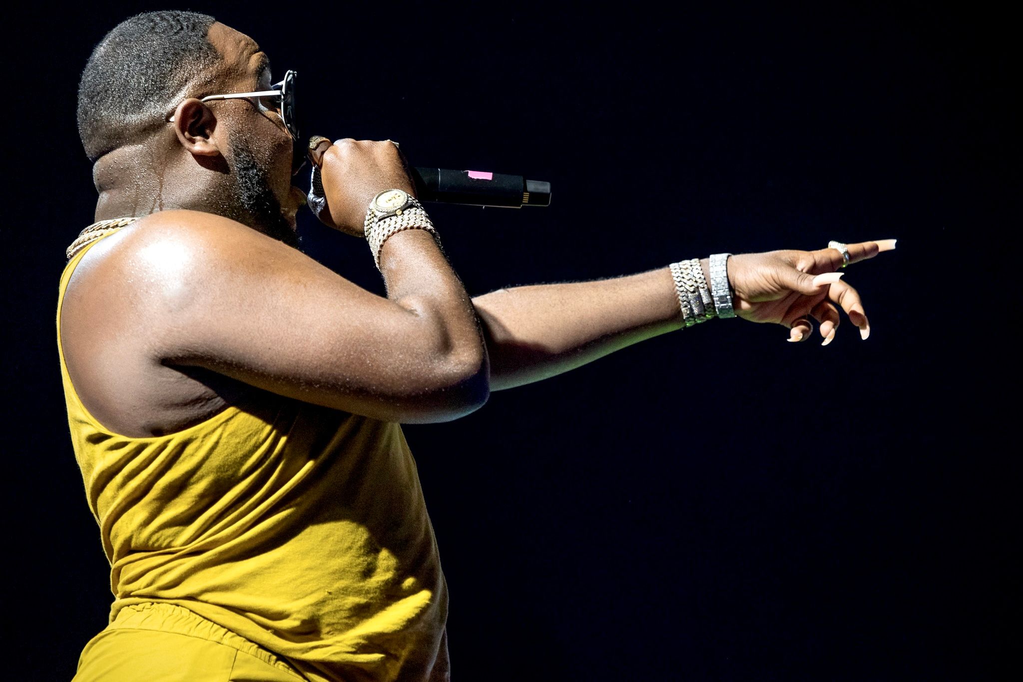 Performer in yellow outfit pointing while singing into microphone during concert.
