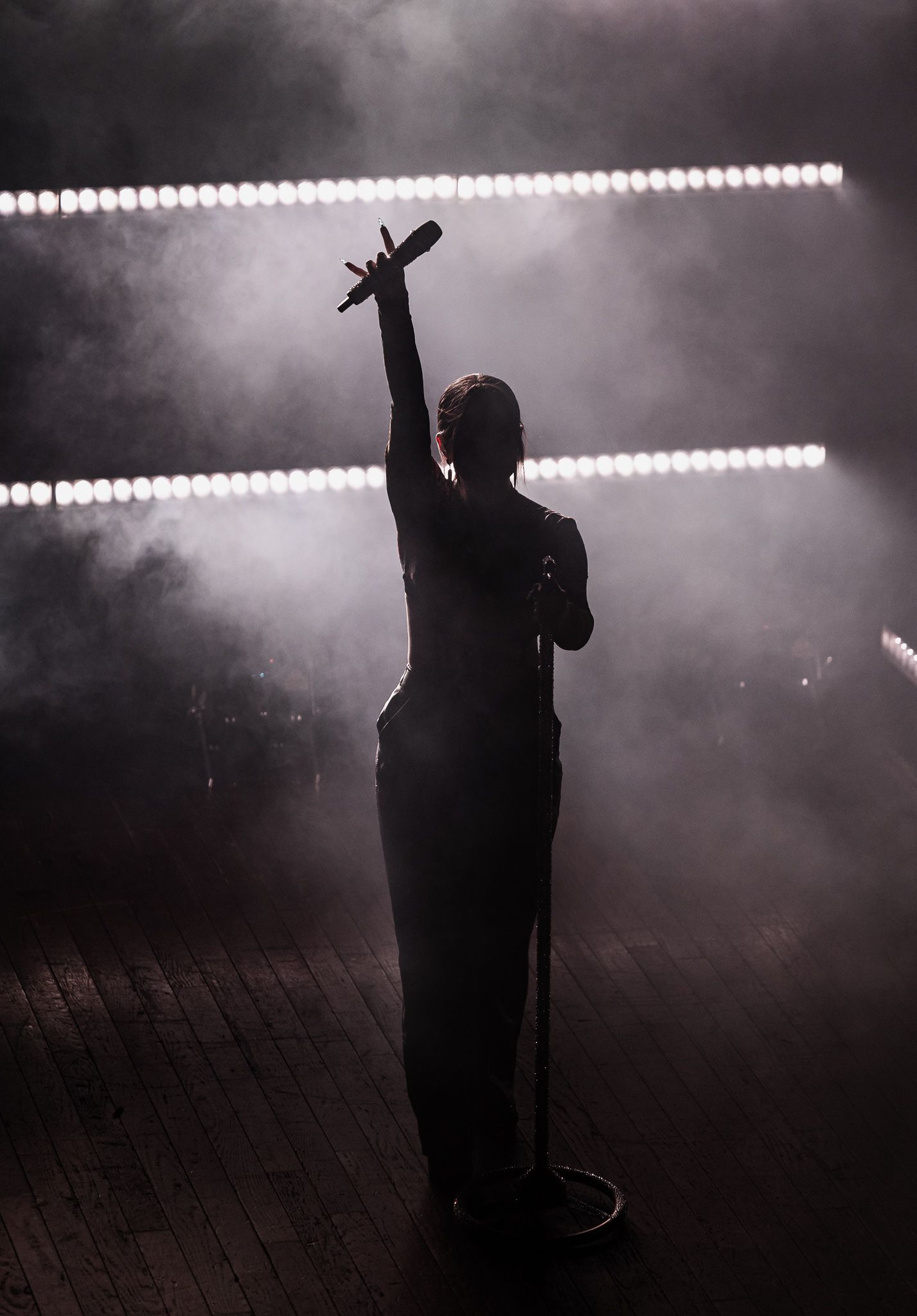 Dramatic silhouette of performer with raised arm against bright stage lights in smoky atmosphere.