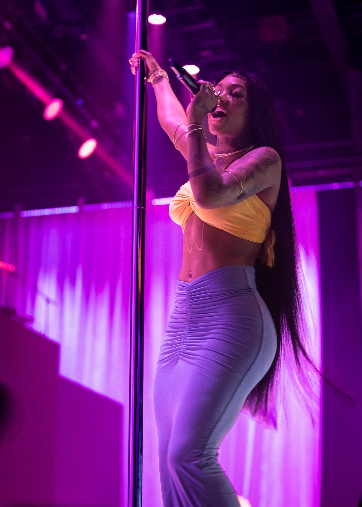 Performer in white outfit dancing with microphone on stage with pink lighting effects.