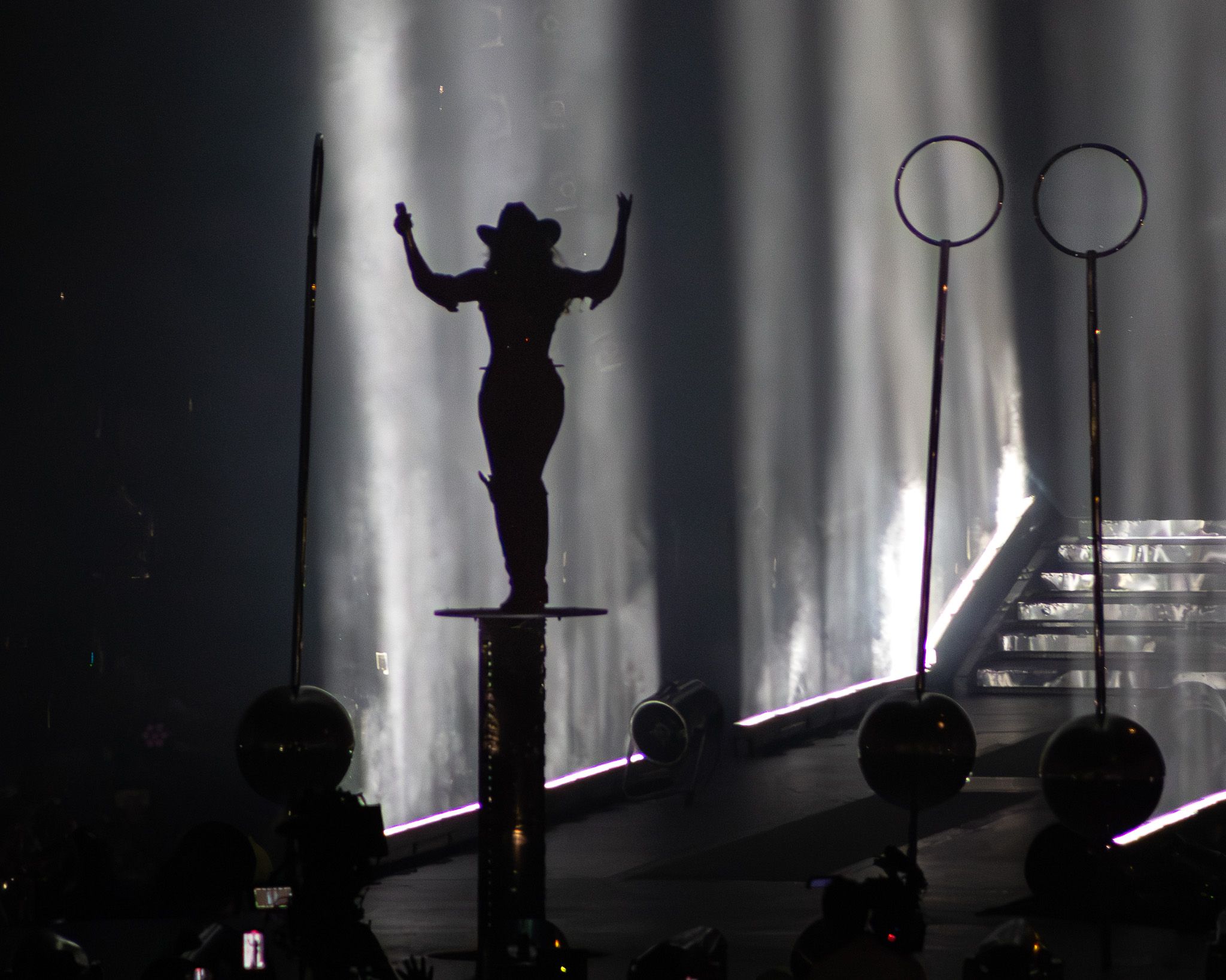 Dramatic silhouette of performer on elevated platform with spotlights and stage equipment.