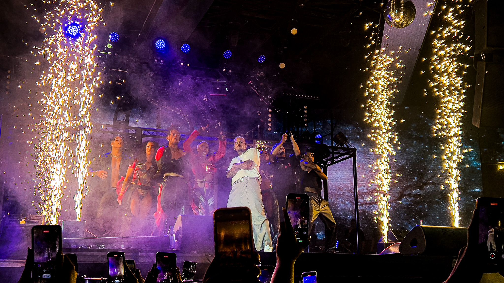 Concert stage with pyrotechnic effects creating golden sparkles against purple backdrop.