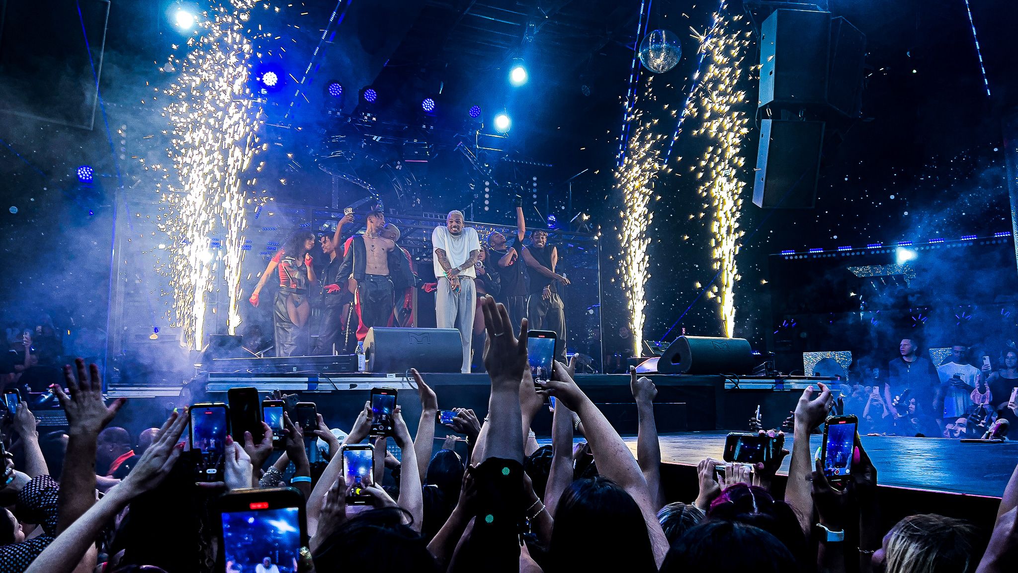 Concert finale with pyrotechnic fountains and crowd reaching towards performer on stage.