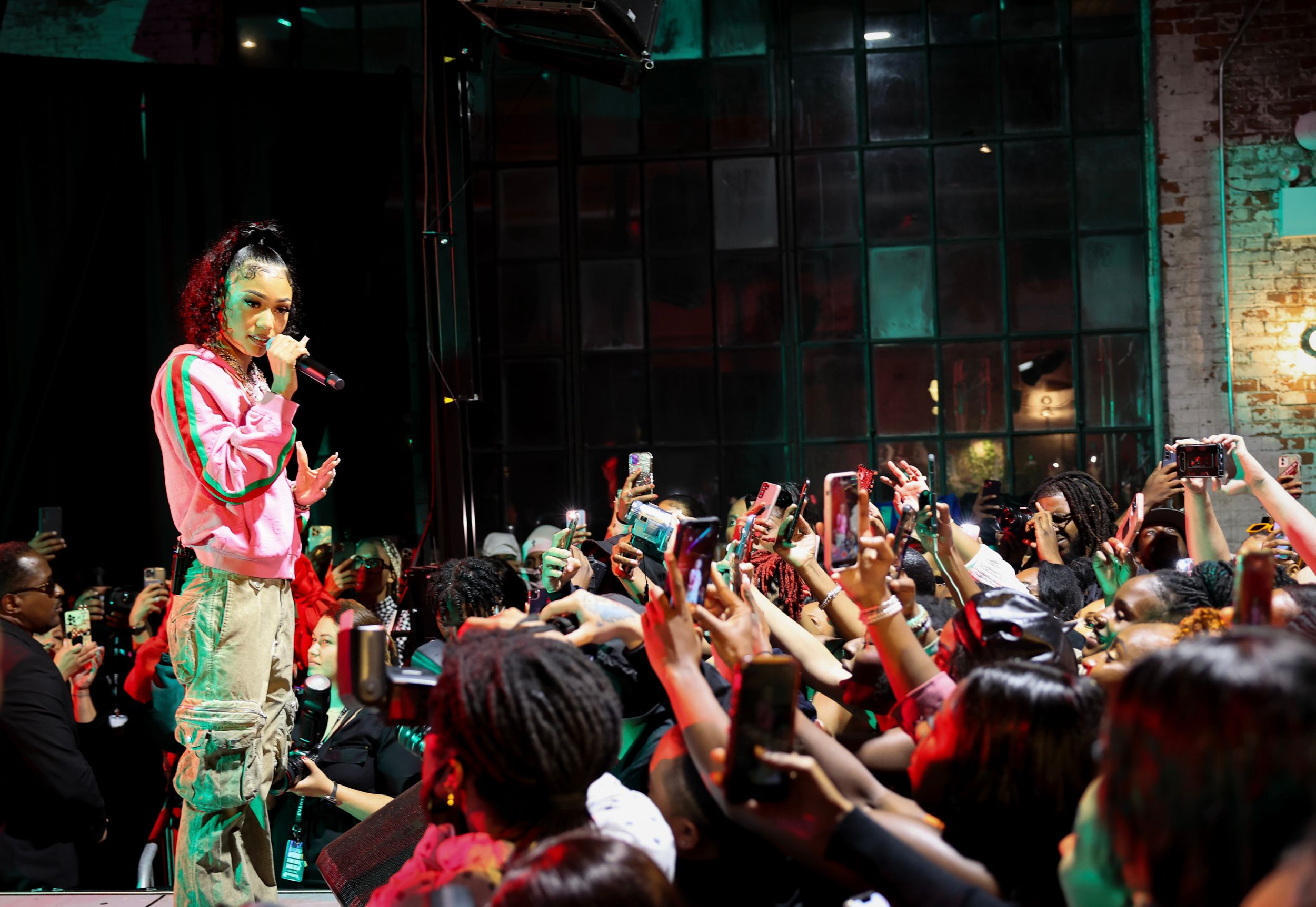 Concert performer in pink outfit on stage with enthusiastic crowd raising hands during live performance.