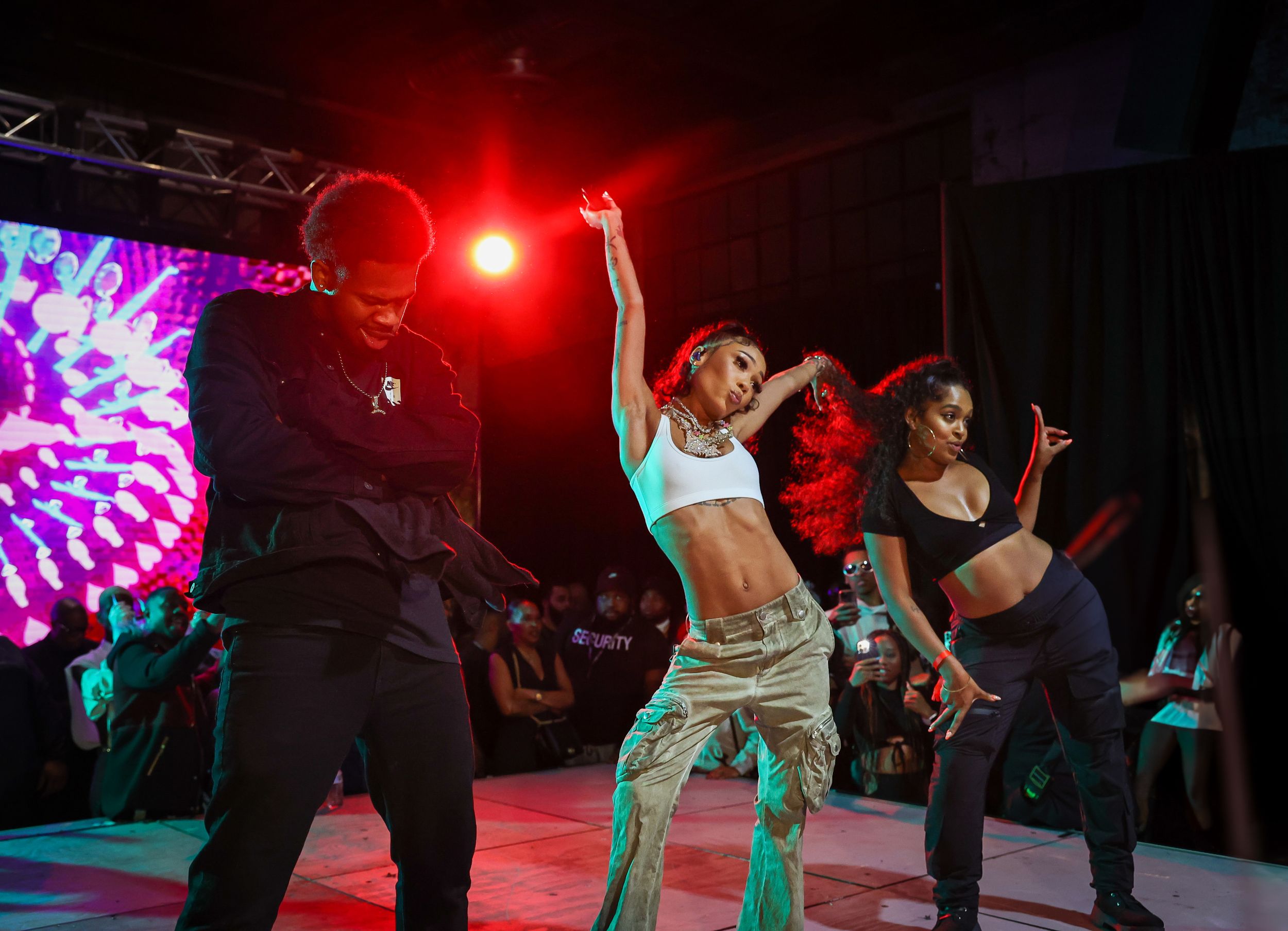Dancers performing choreographed routine on stage with red lighting and psychedelic backdrop.