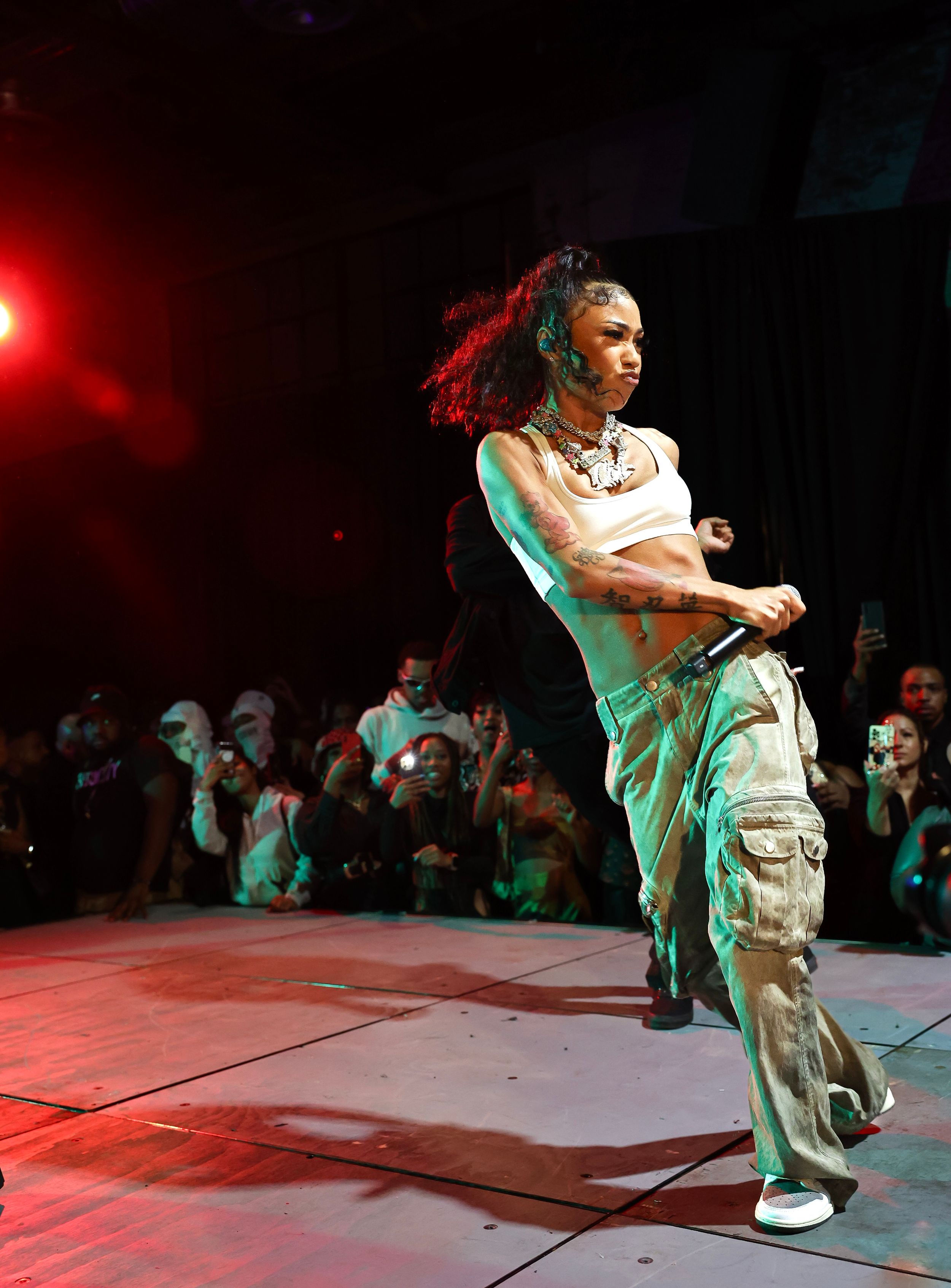 Dancer strikes dynamic pose in cargo pants and crop top on red-lit concert stage.