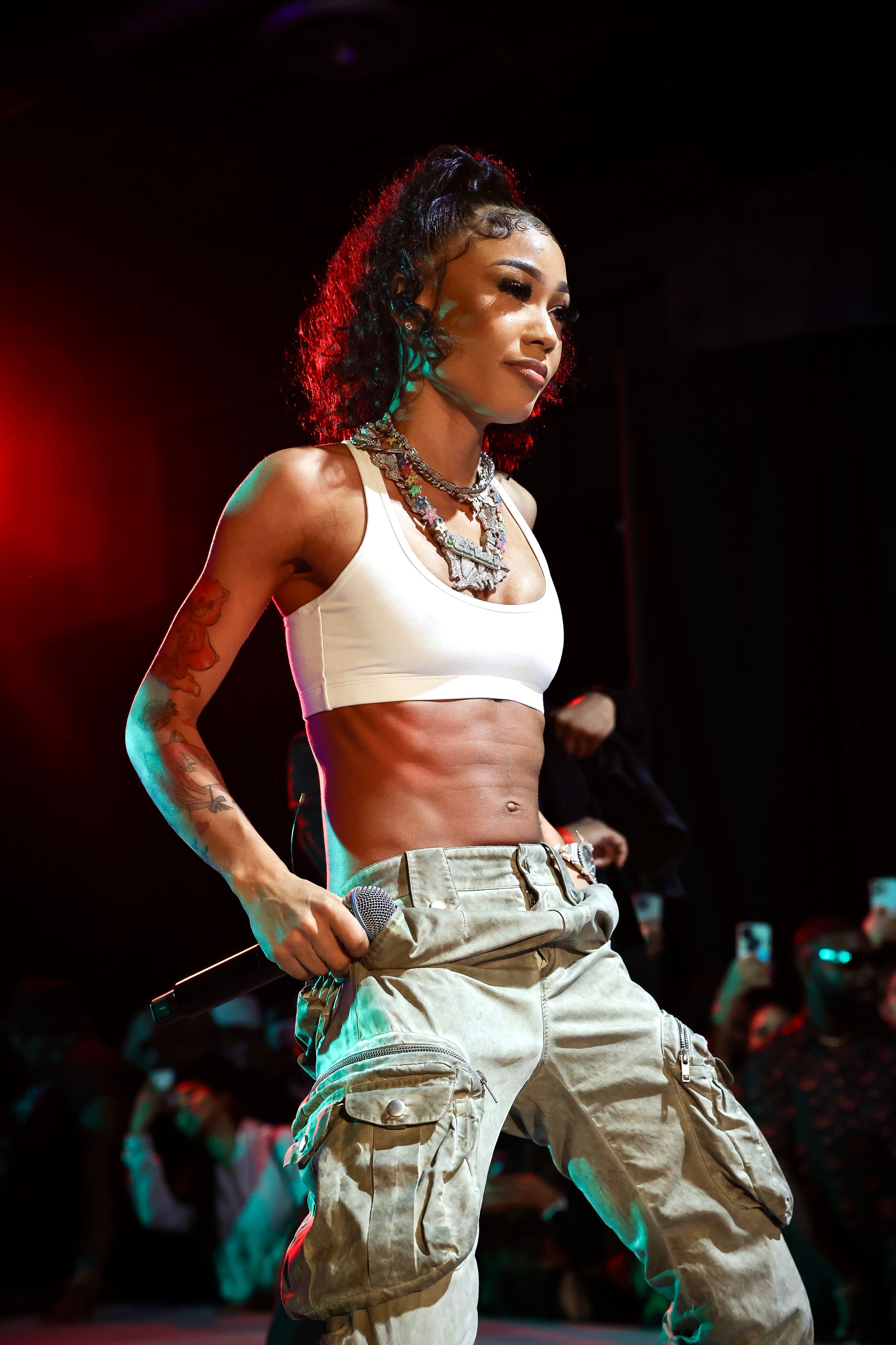 Performer in white crop top and cargo pants dances energetically on concert stage.