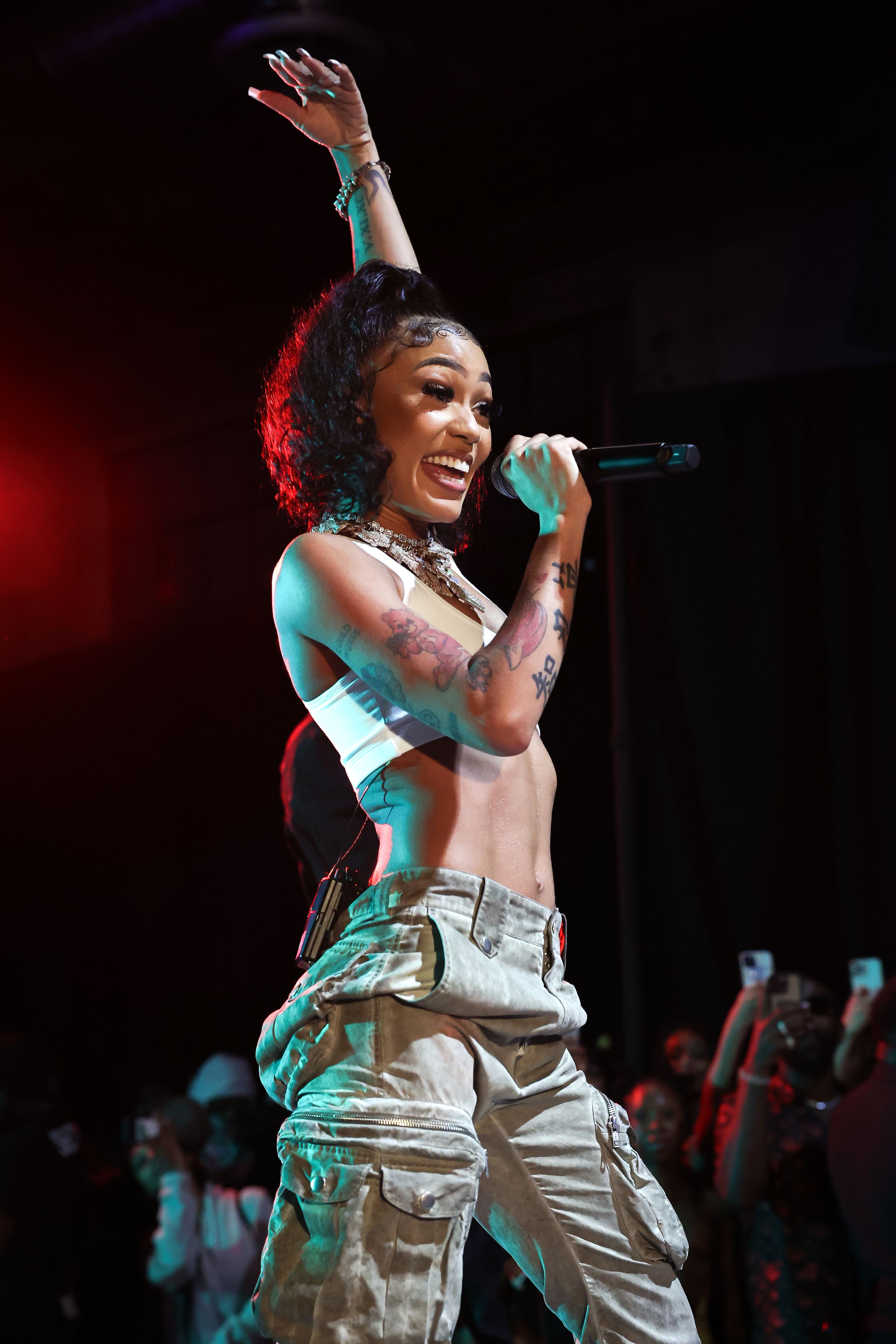 Energetic stage performance with performer in white top and cargo pants under colored lights.