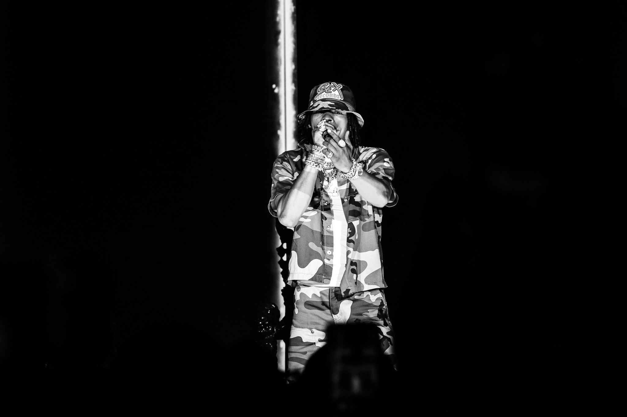 Dramatic black and white shot of performer in camo gear on illuminated stage.
