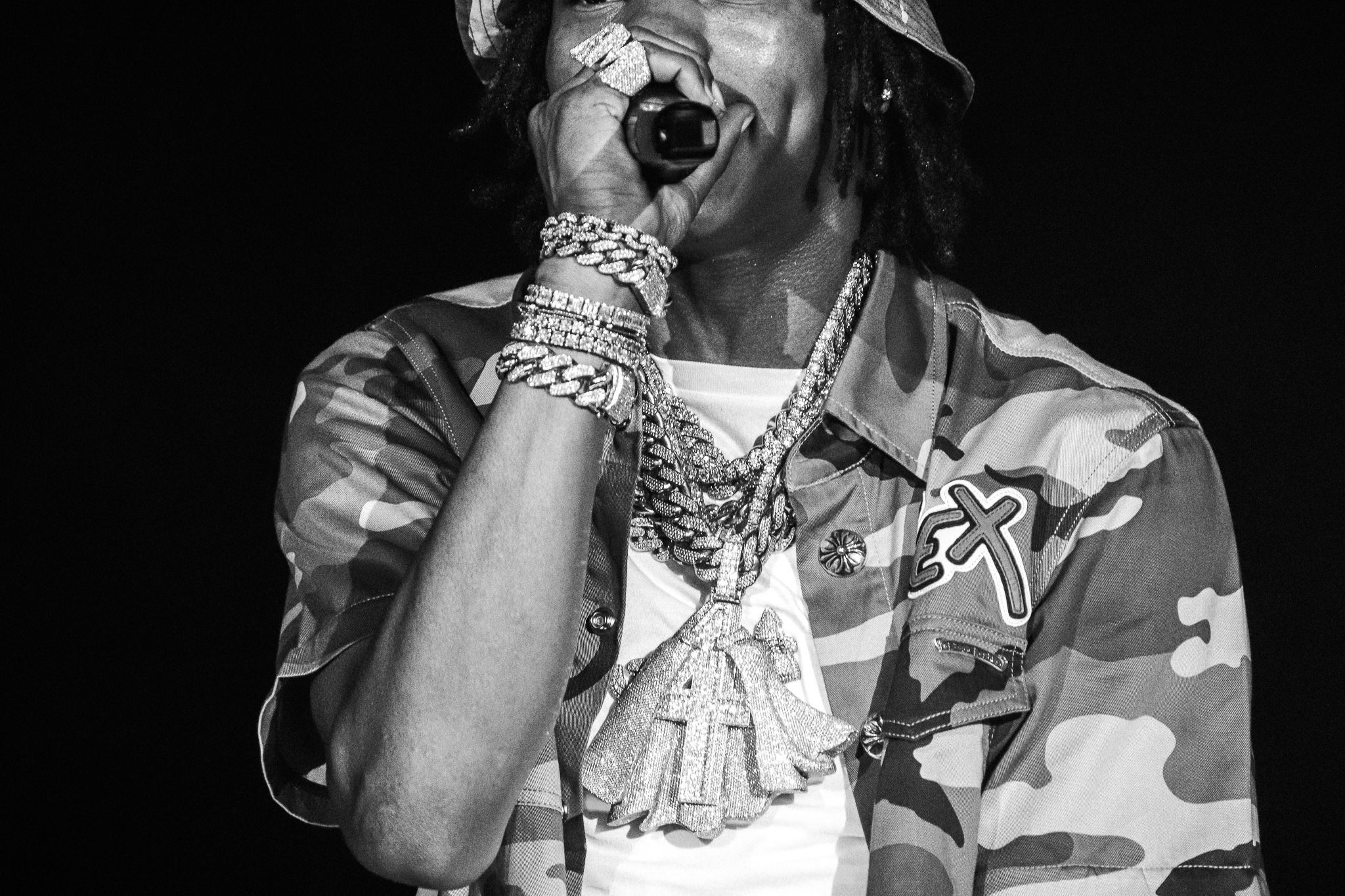 Performer in camouflage outfit with jewelry performing on stage in black and white.