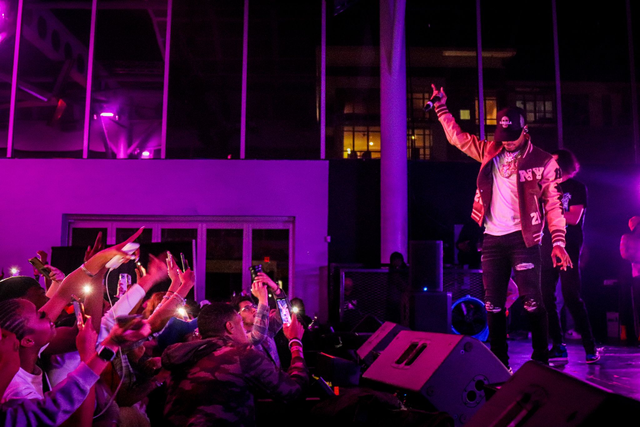 Concert performers energetically entertaining crowd under vibrant purple lighting on elevated stage.