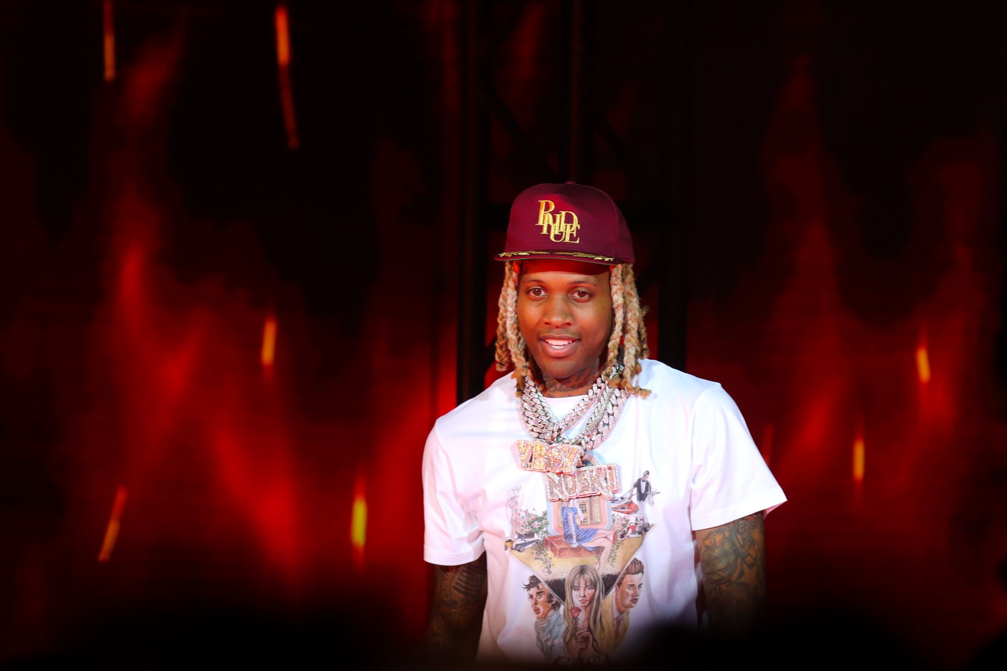 Performer in white t-shirt and red cap against dramatic red lighting background.