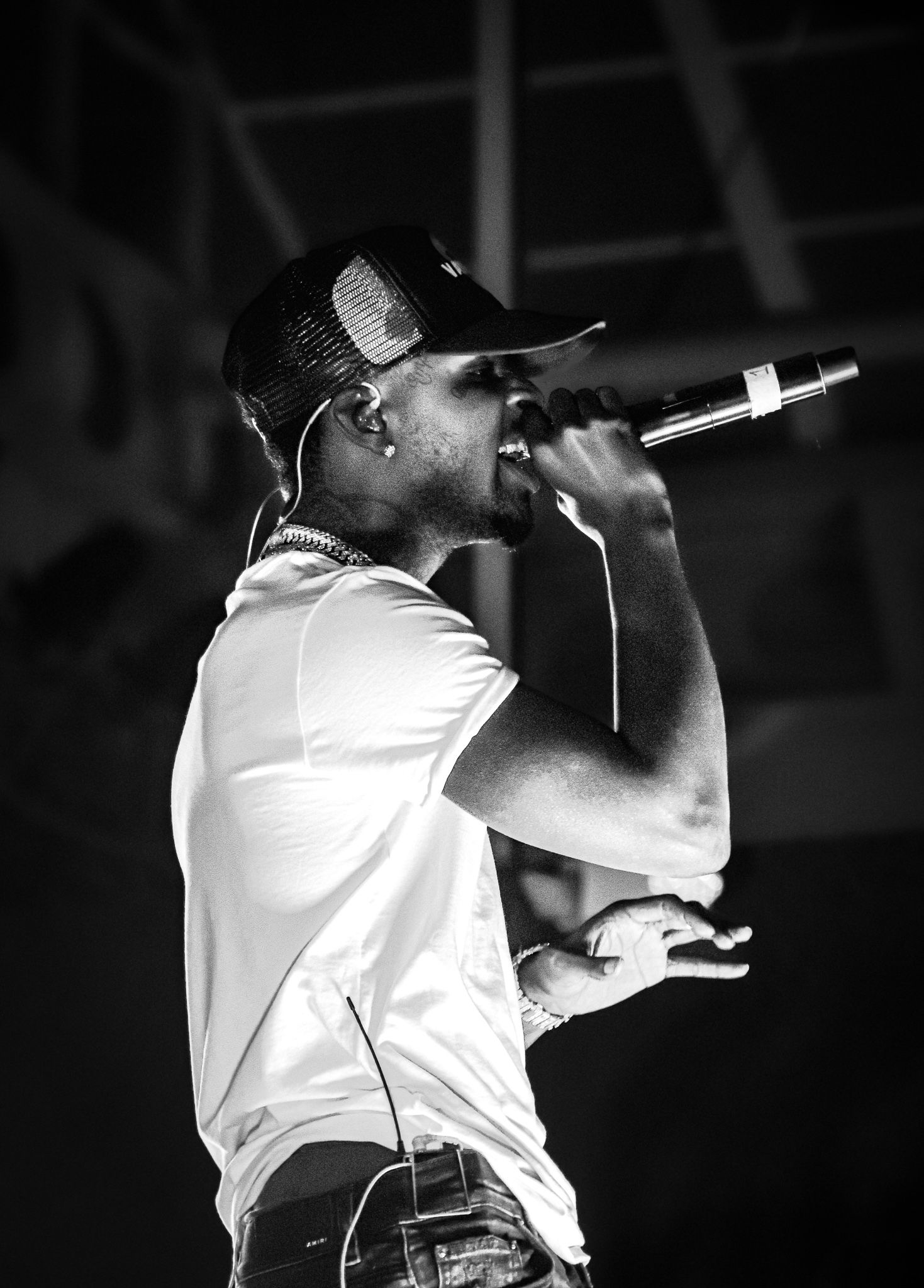 Black and white photo of performer in white shirt and cap singing passionately into microphone.