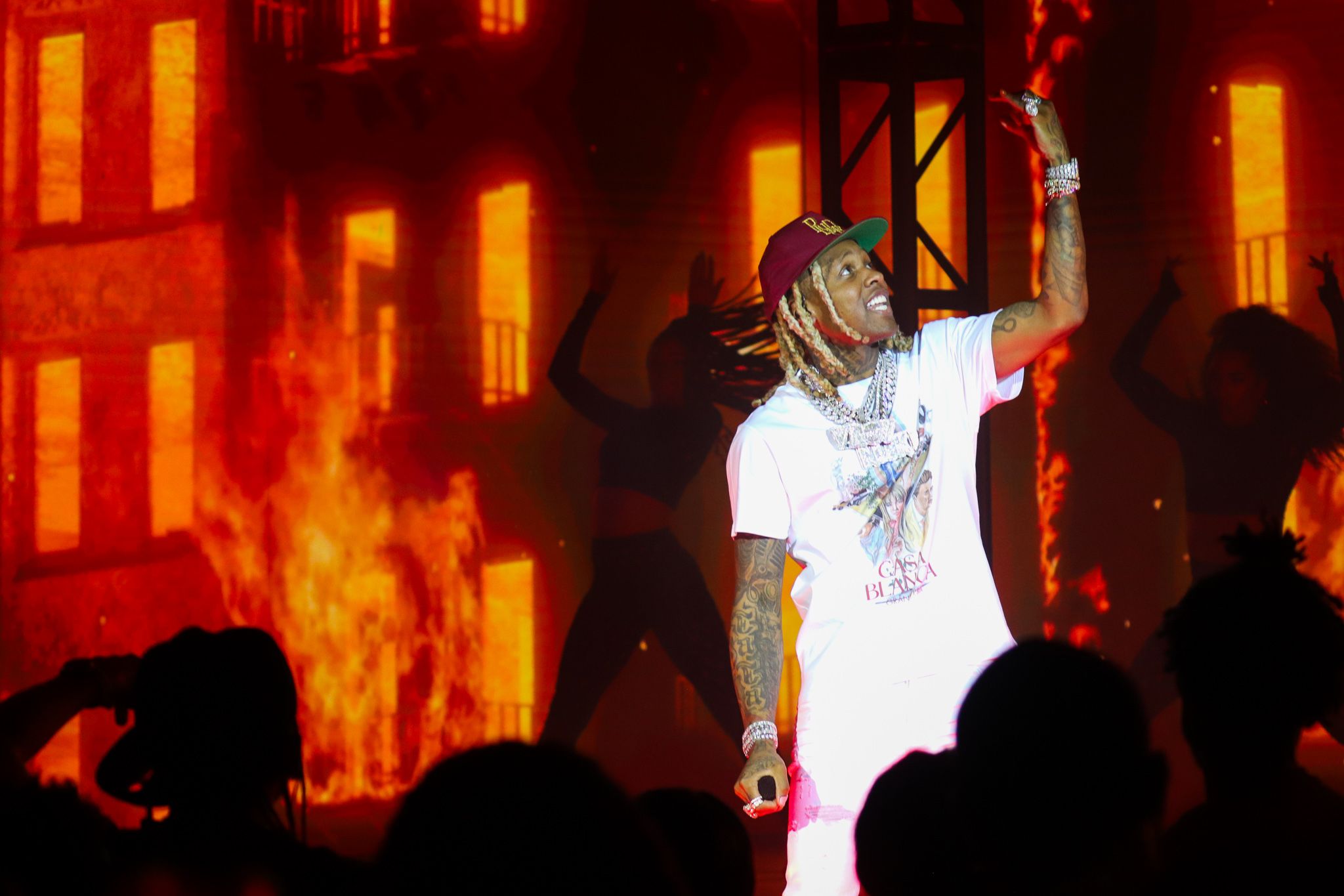Stage performer in white outfit energetically performs against fiery orange backdrop.