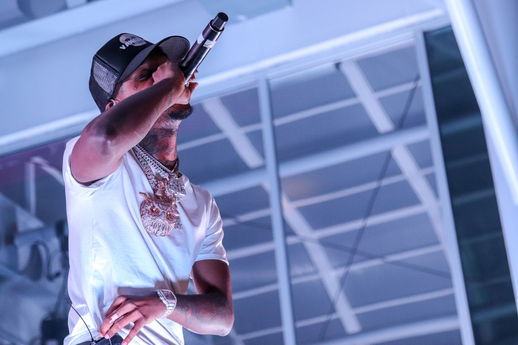 Performer in white shirt and cap singing under blue stage lighting.