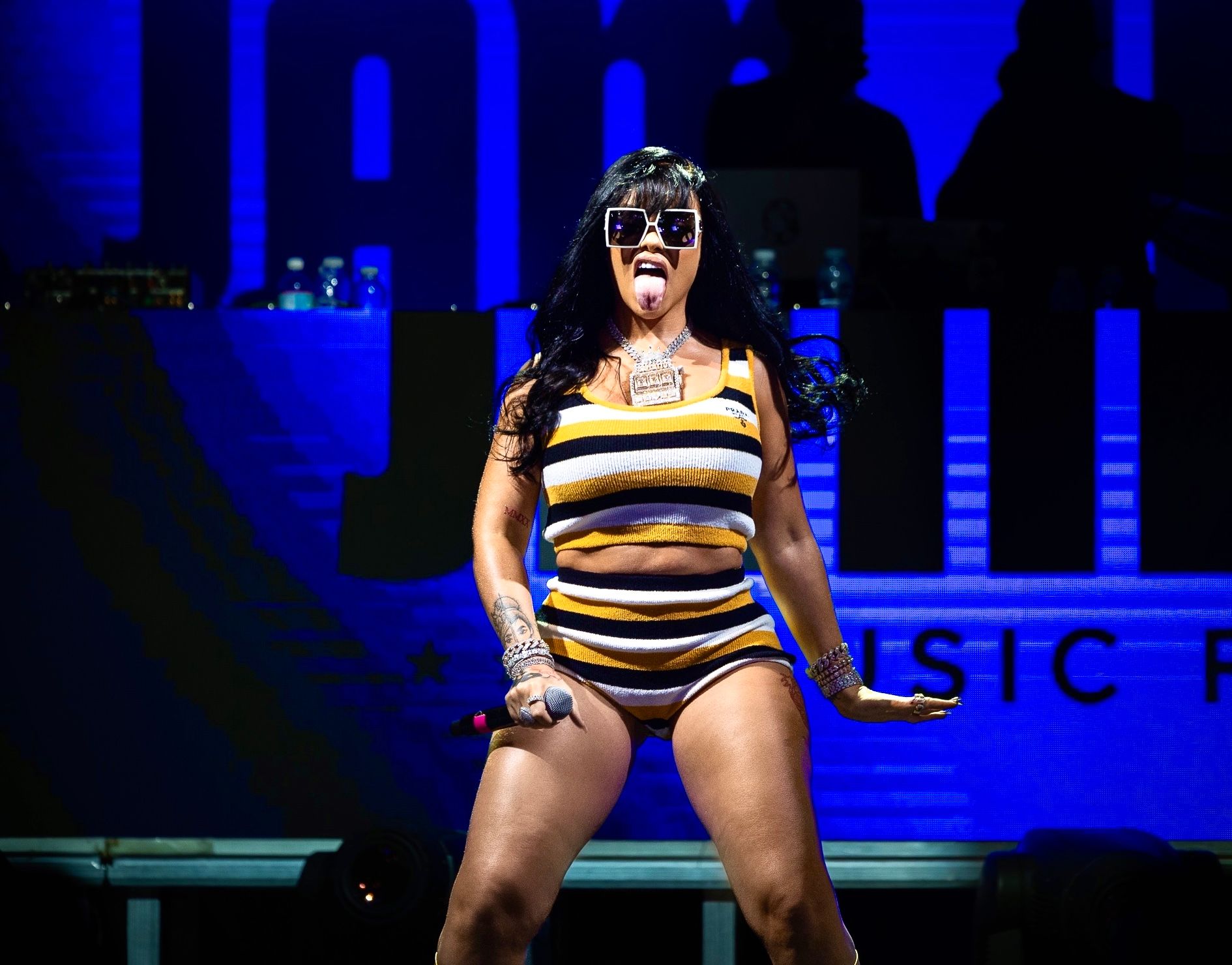 Performer in striped swimsuit dancing on stage under blue lighting at concert performance.