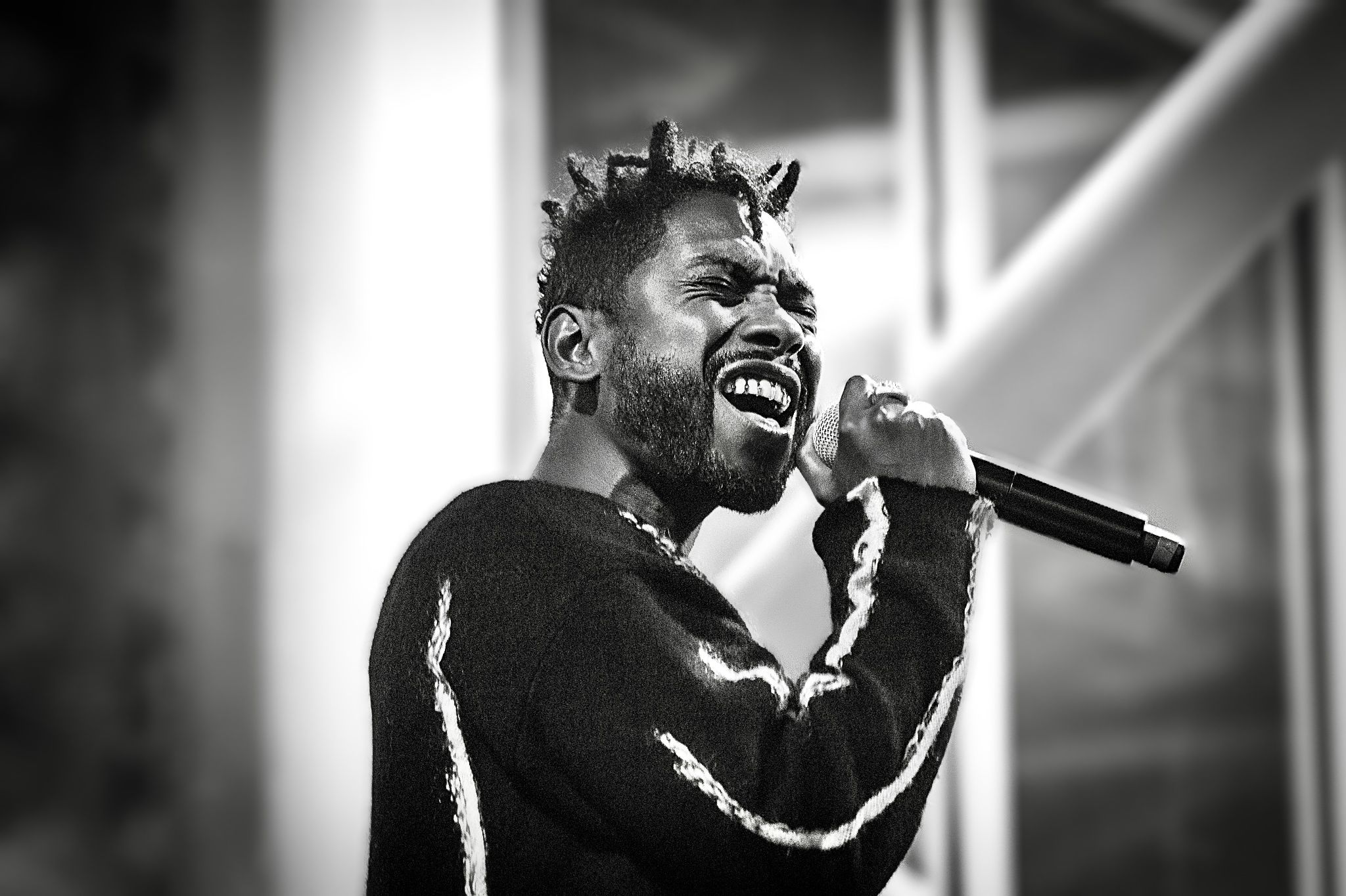 An energetic performer singing with passion on stage in black and white.