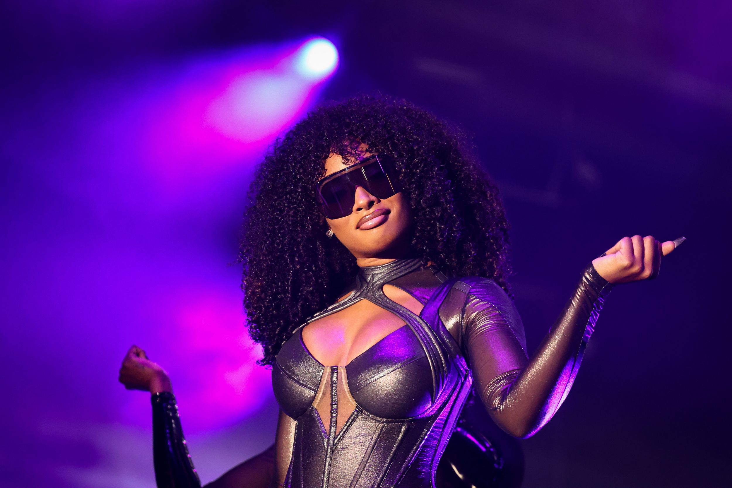 Performer in metallic outfit singing during concert with purple stage lighting.