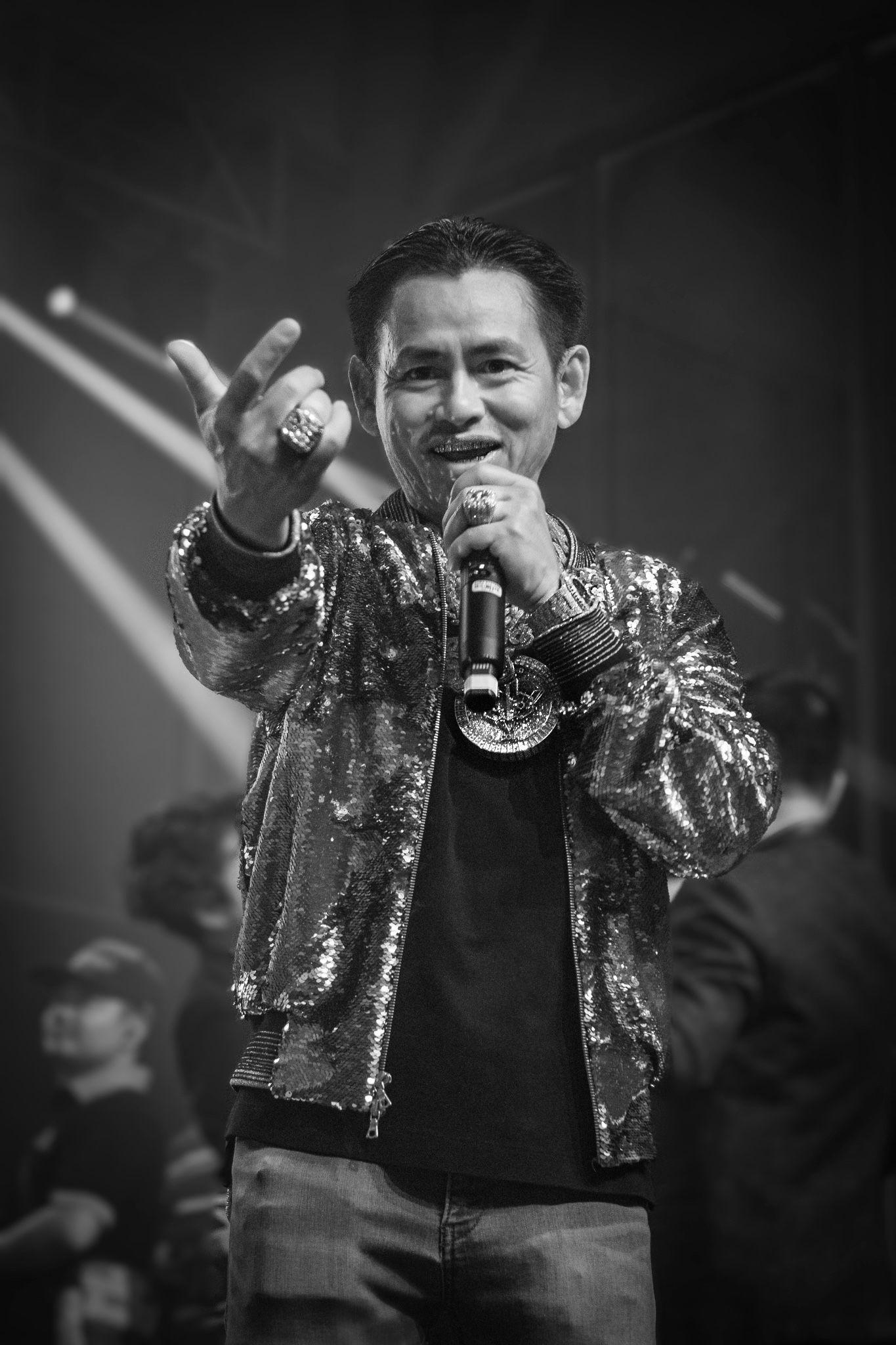 Performer in sparkly jacket sings passionately on stage during black and white concert photo.