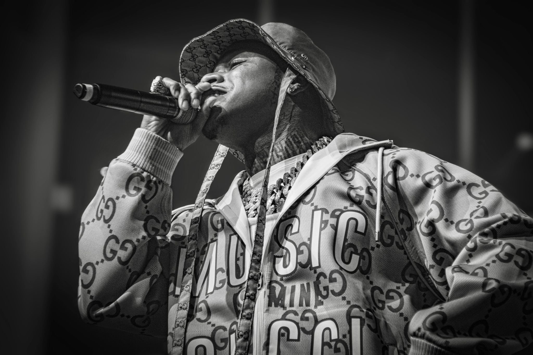 Hip hop artist performs on stage wearing designer hoodie in dramatic monochrome lighting.