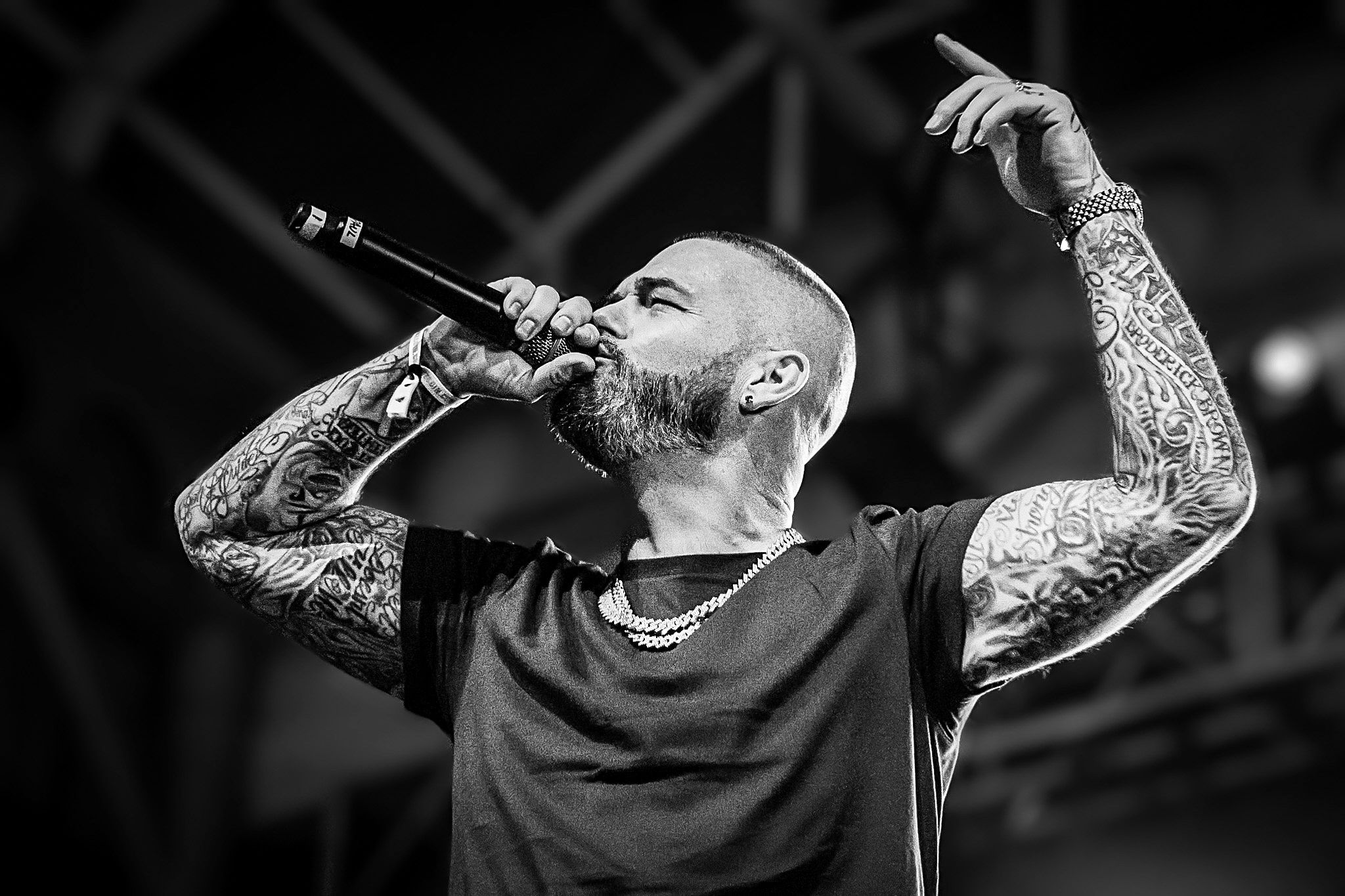 Tattooed vocalist passionately performs on stage in black and white concert photograph.
