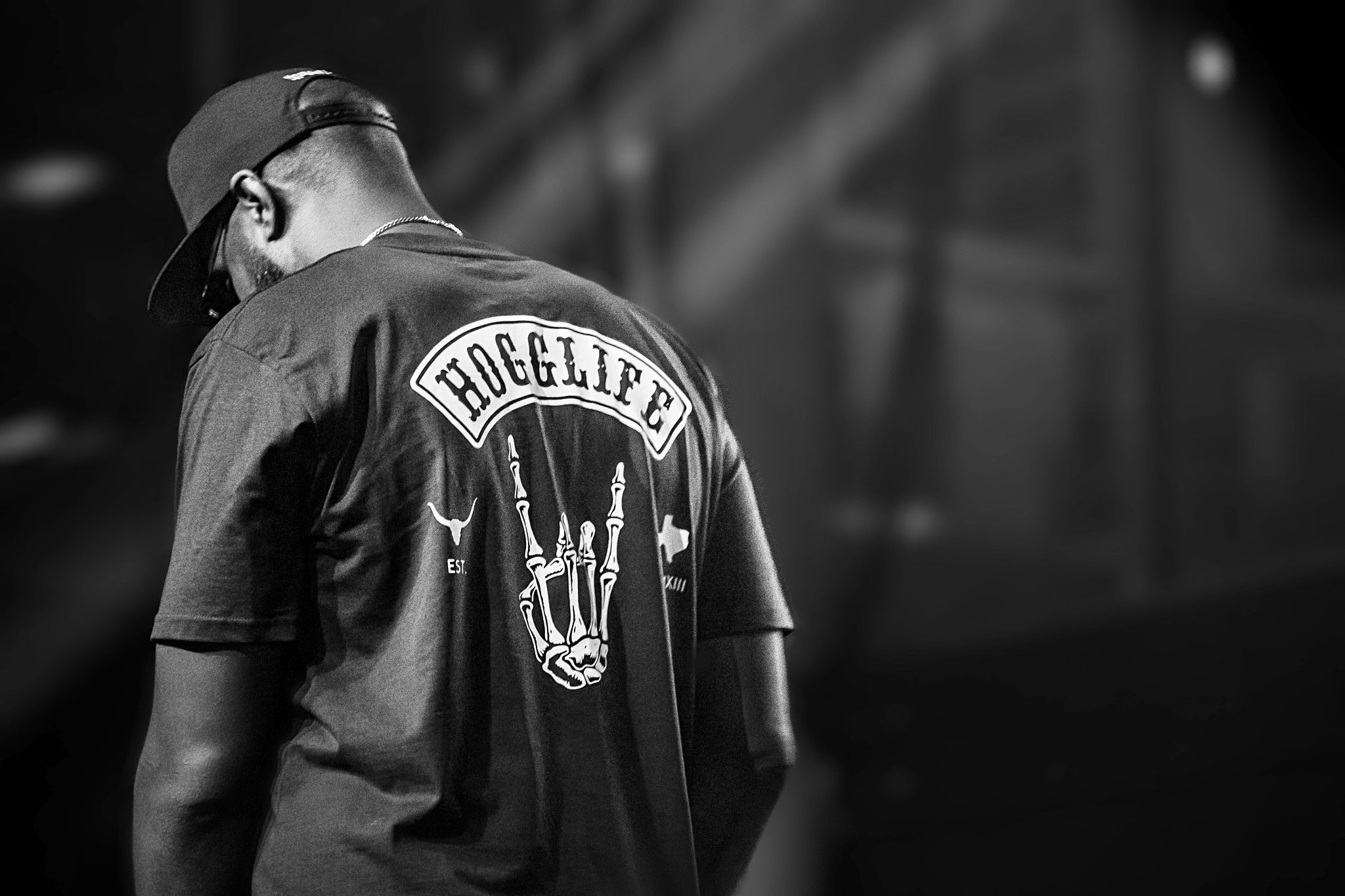 Black and white photo of someone wearing a rock band t-shirt with metal horns symbol viewed from behind.