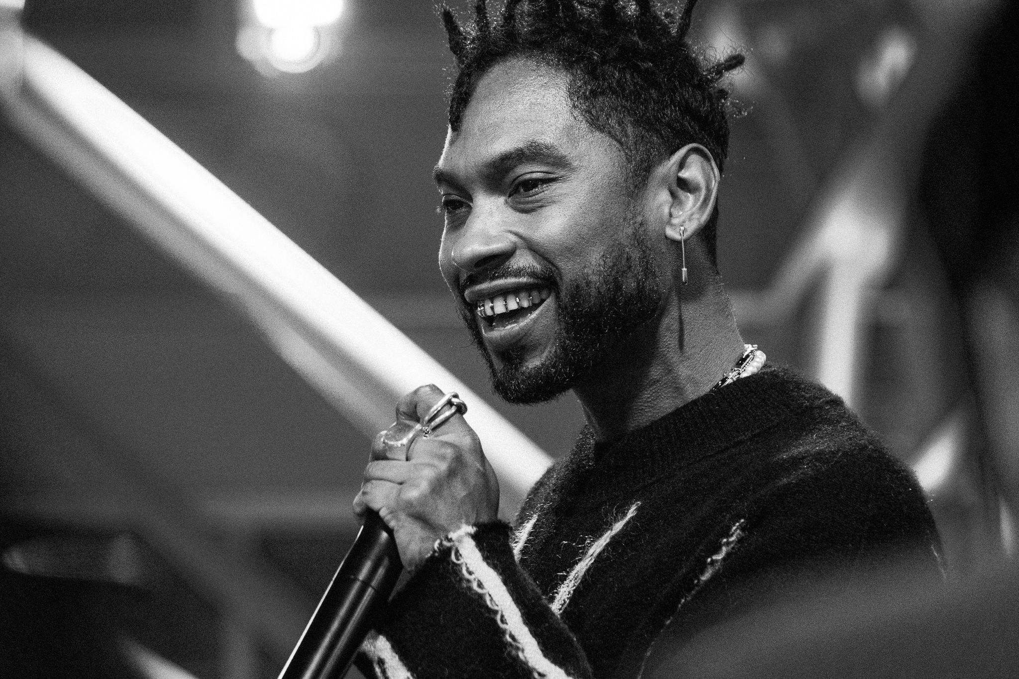 Black and white portrait of smiling performer holding microphone during show.