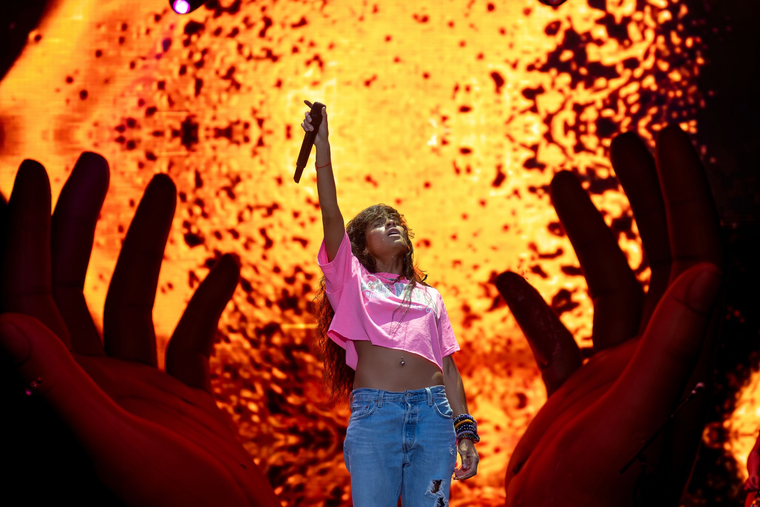 Dramatic concert scene with performer silhouetted against orange backdrop and giant hands.