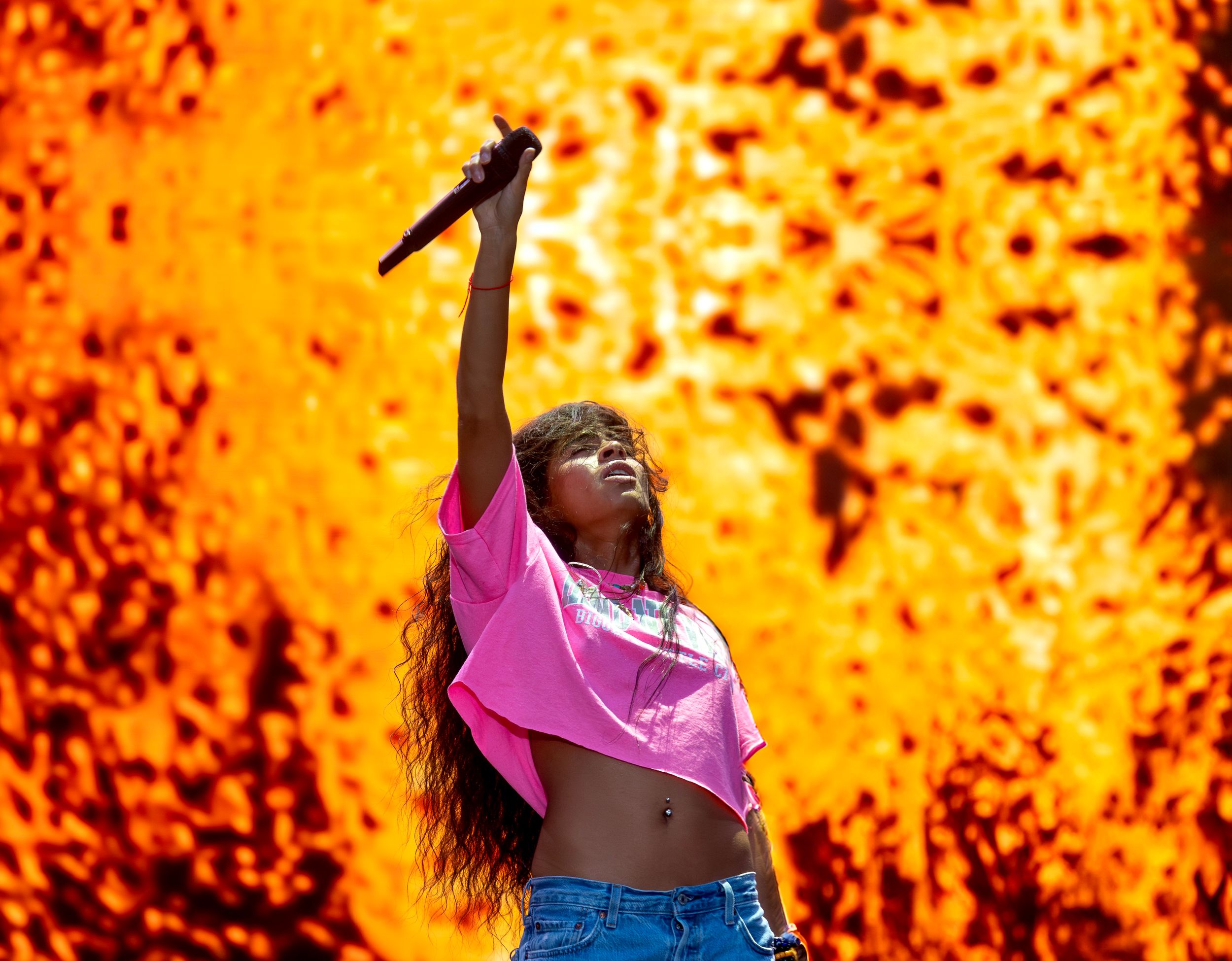 Dynamic concert shot with performer in pink top against vibrant orange pyrotechnic background.