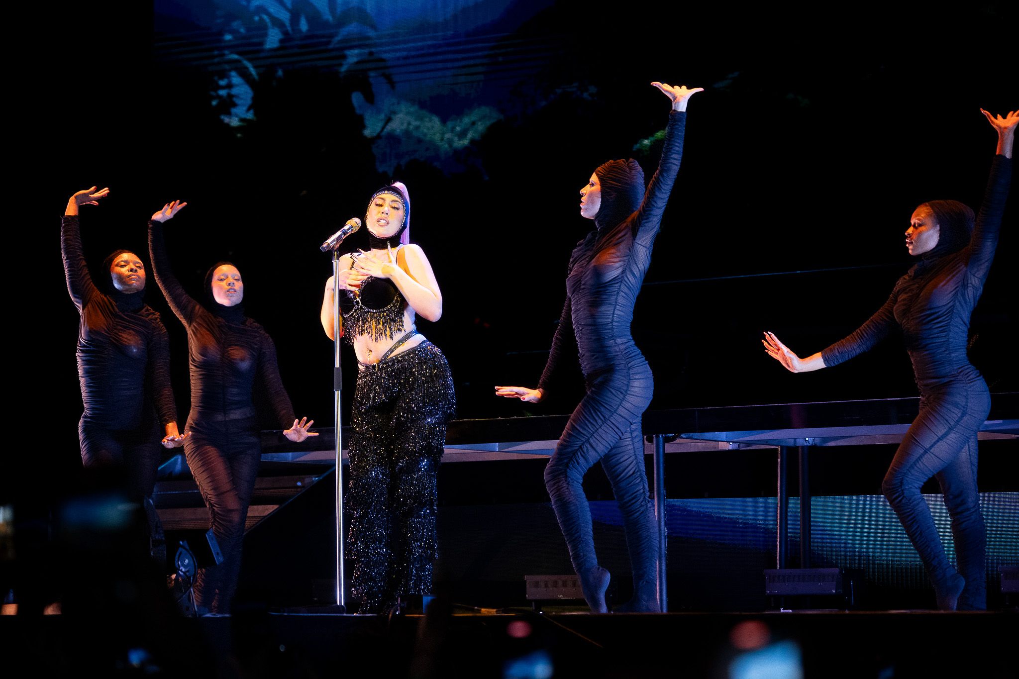 Dramatic concert performance with dancers in dark outfits on elevated platforms.