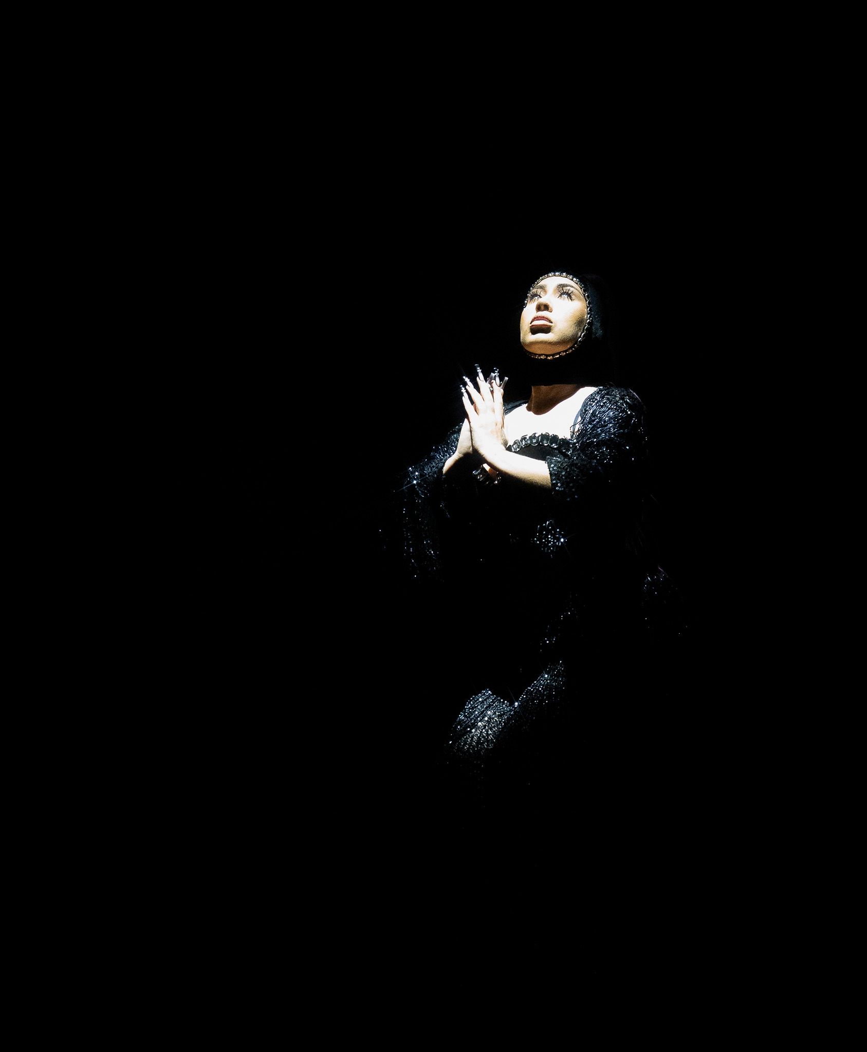 Dramatic spotlight performance with artist in dark attire against black background.