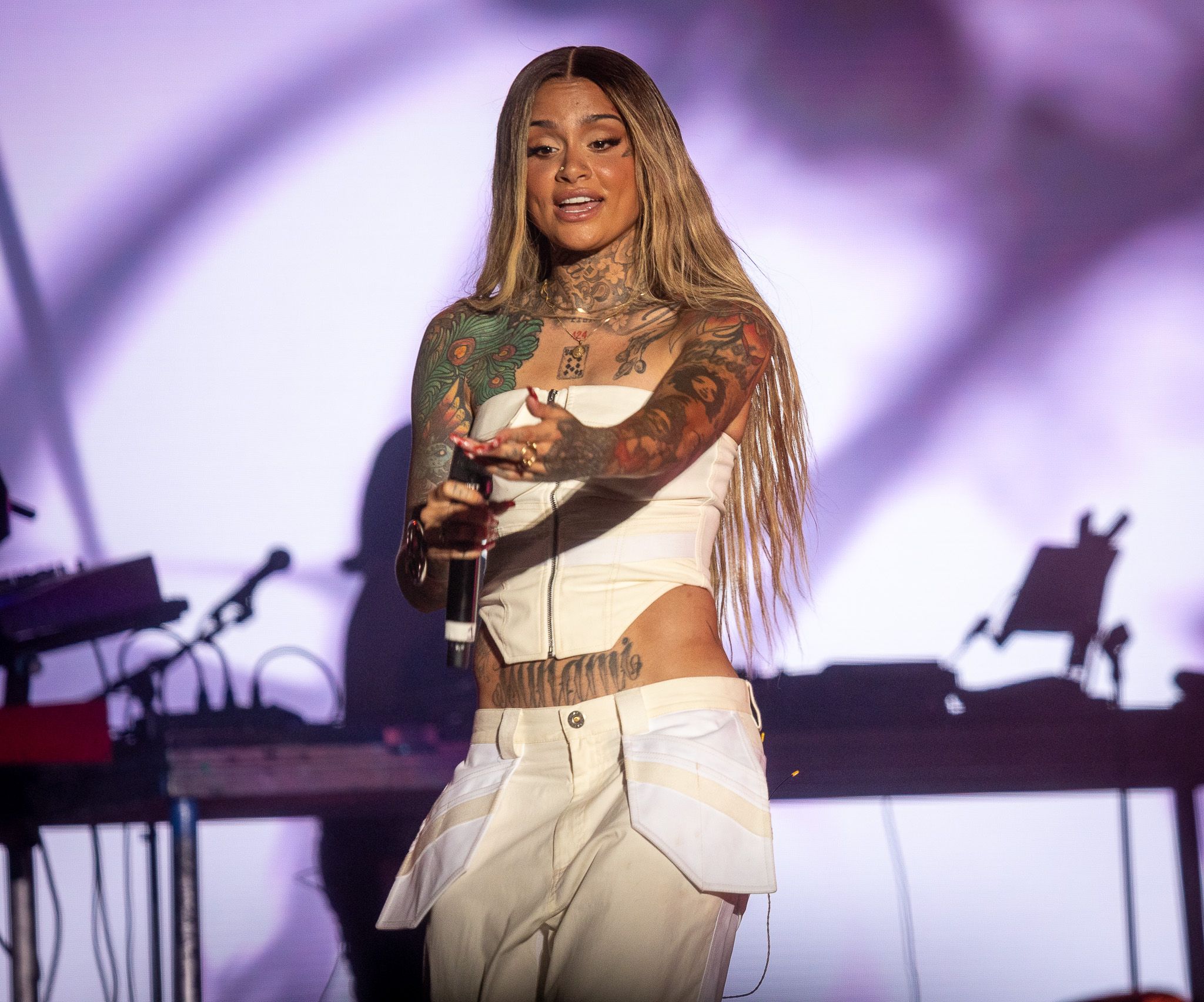 Concert performer in white outfit on stage with purple lighting effects.