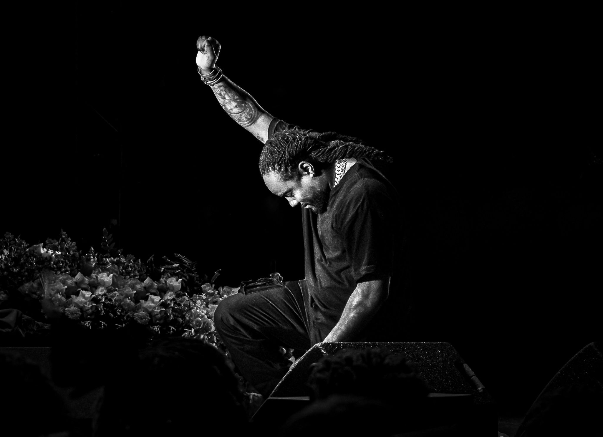 Dramatic black and white shot of a performer on stage with raised arm in silhouette.