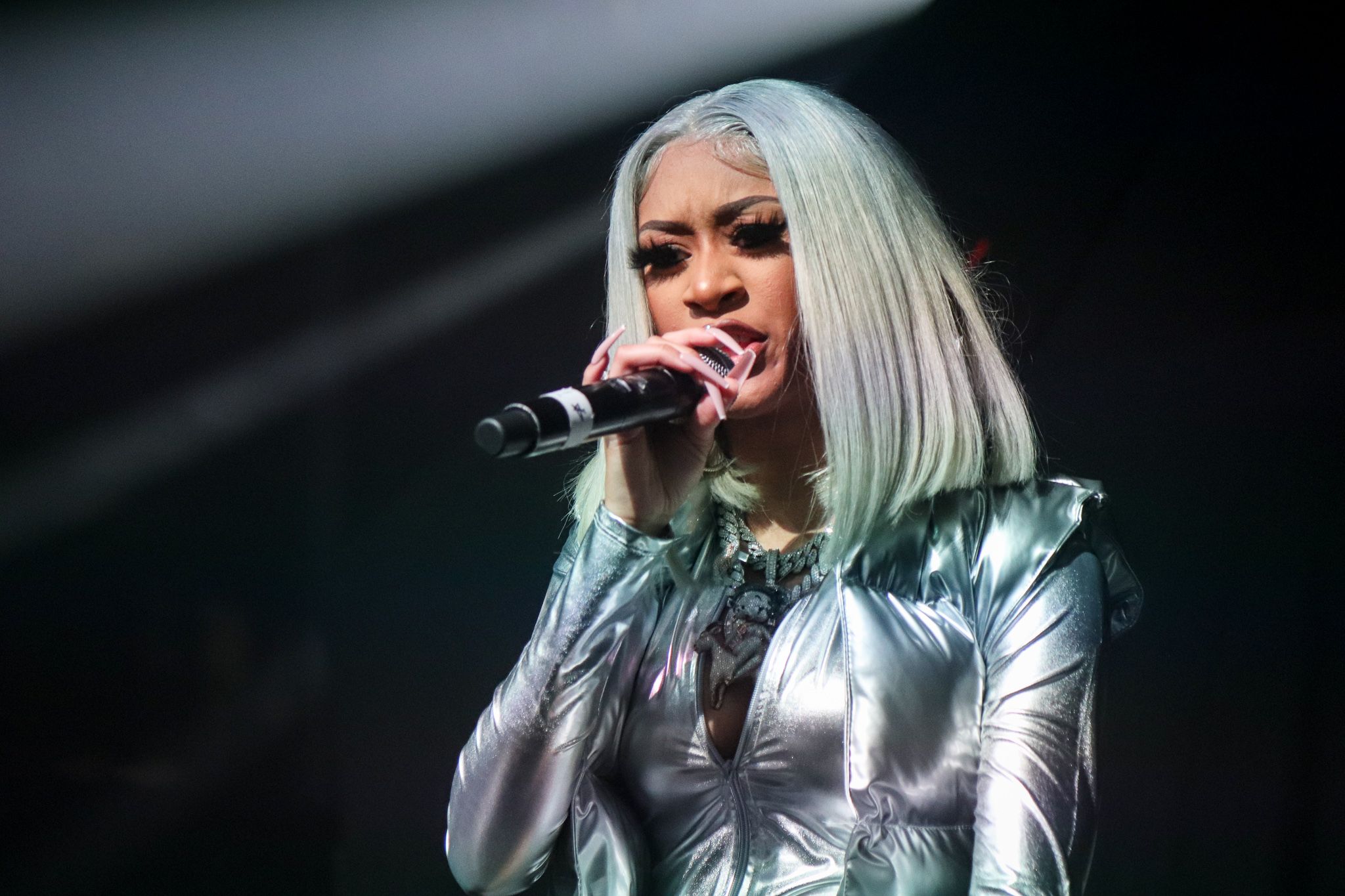 Performer in silver metallic outfit singing with microphone during stage performance.